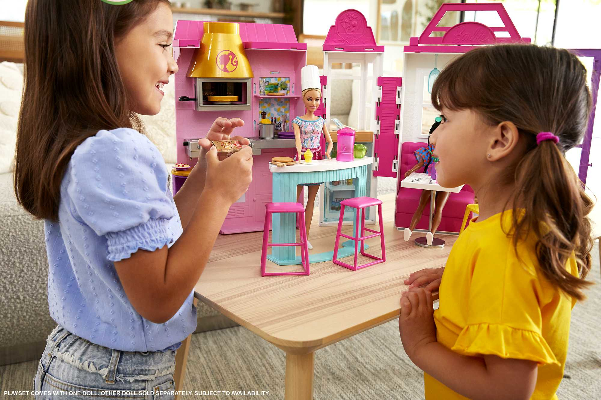 Due ragazze giocano con il set da cucina di Barbie. Bambola Barbie che cucina. Mobili da cucina, sgabelli rosa.