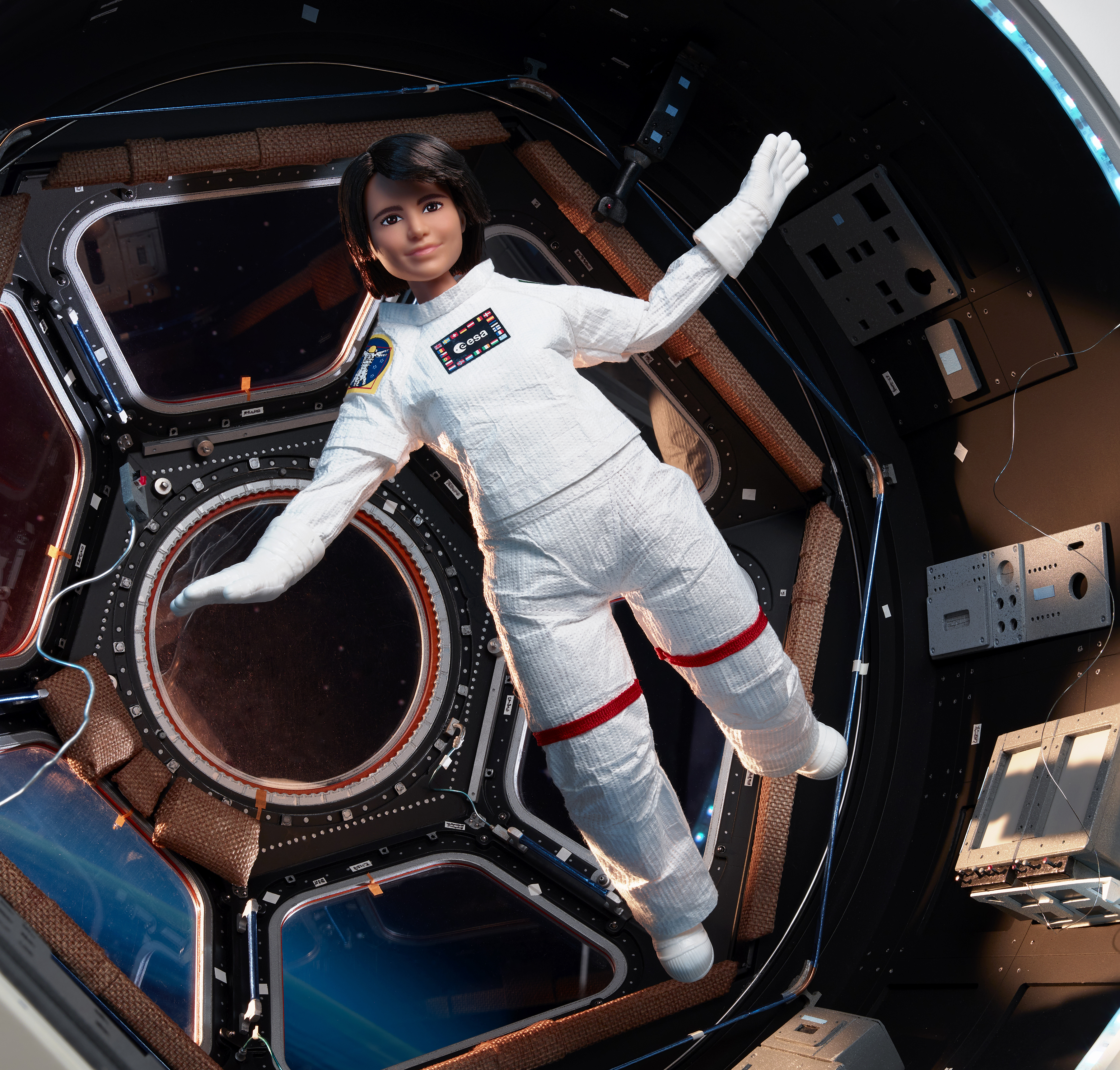 Una muñeca con un traje espacial flota dentro de una estación espacial. Se ve el interior de la estación.