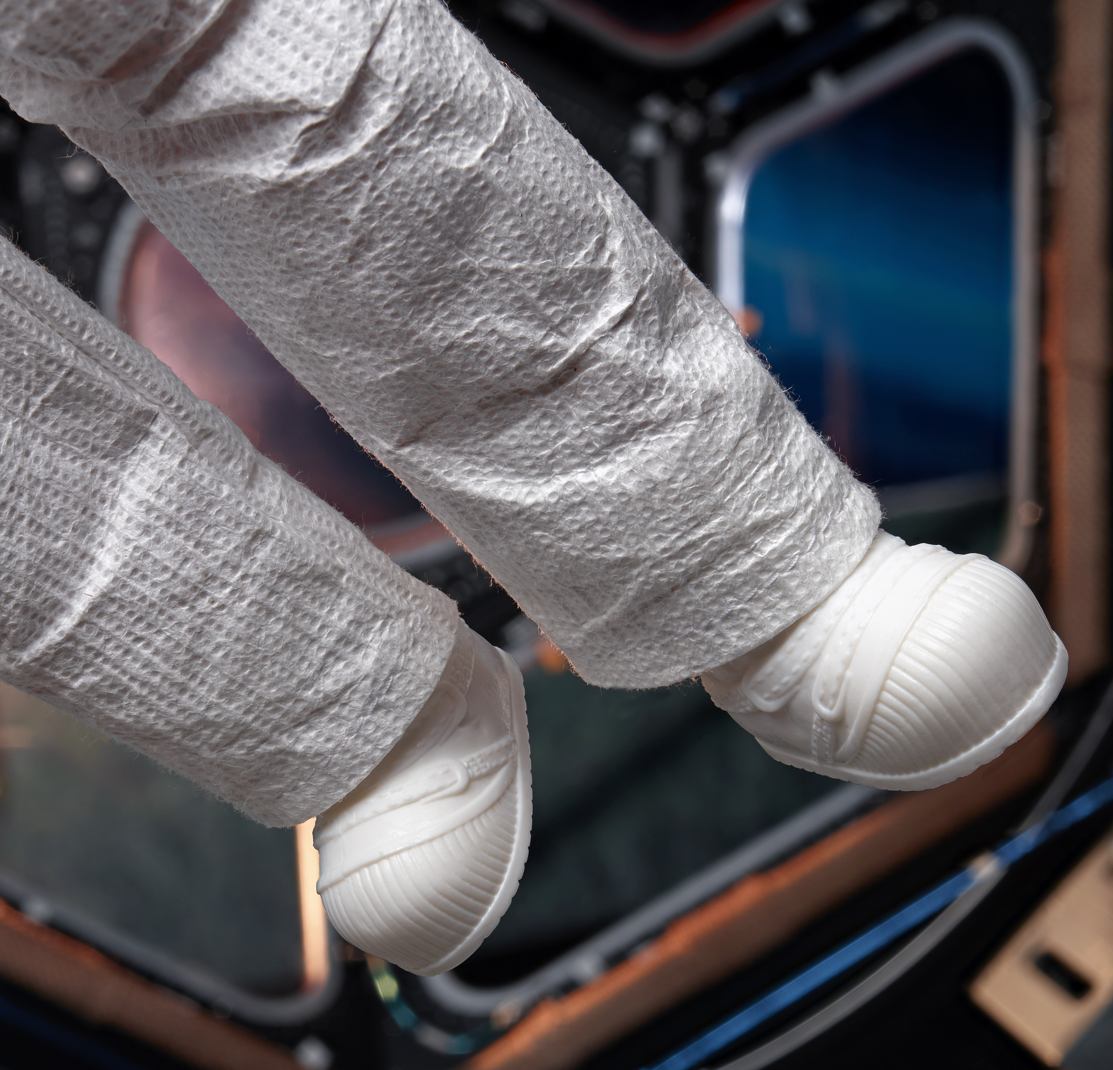 Piernas de astronauta con botas blancas de traje espacial, flotando en el interior de una estación espacial.