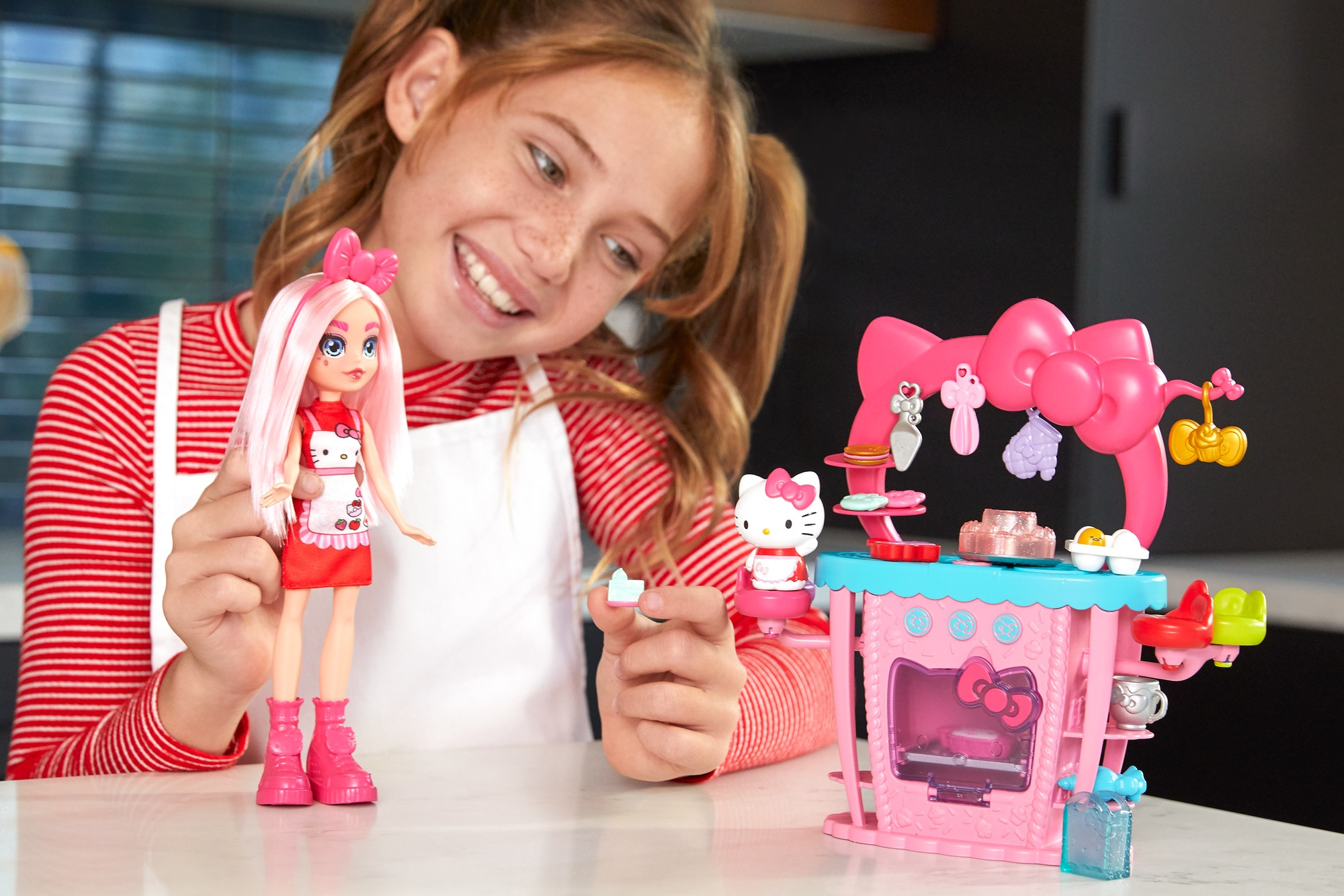 Una ragazza con una bambola e un set da cucina giocattolo. Il giocattolo è rosa con dettagli di Hello Kitty.
