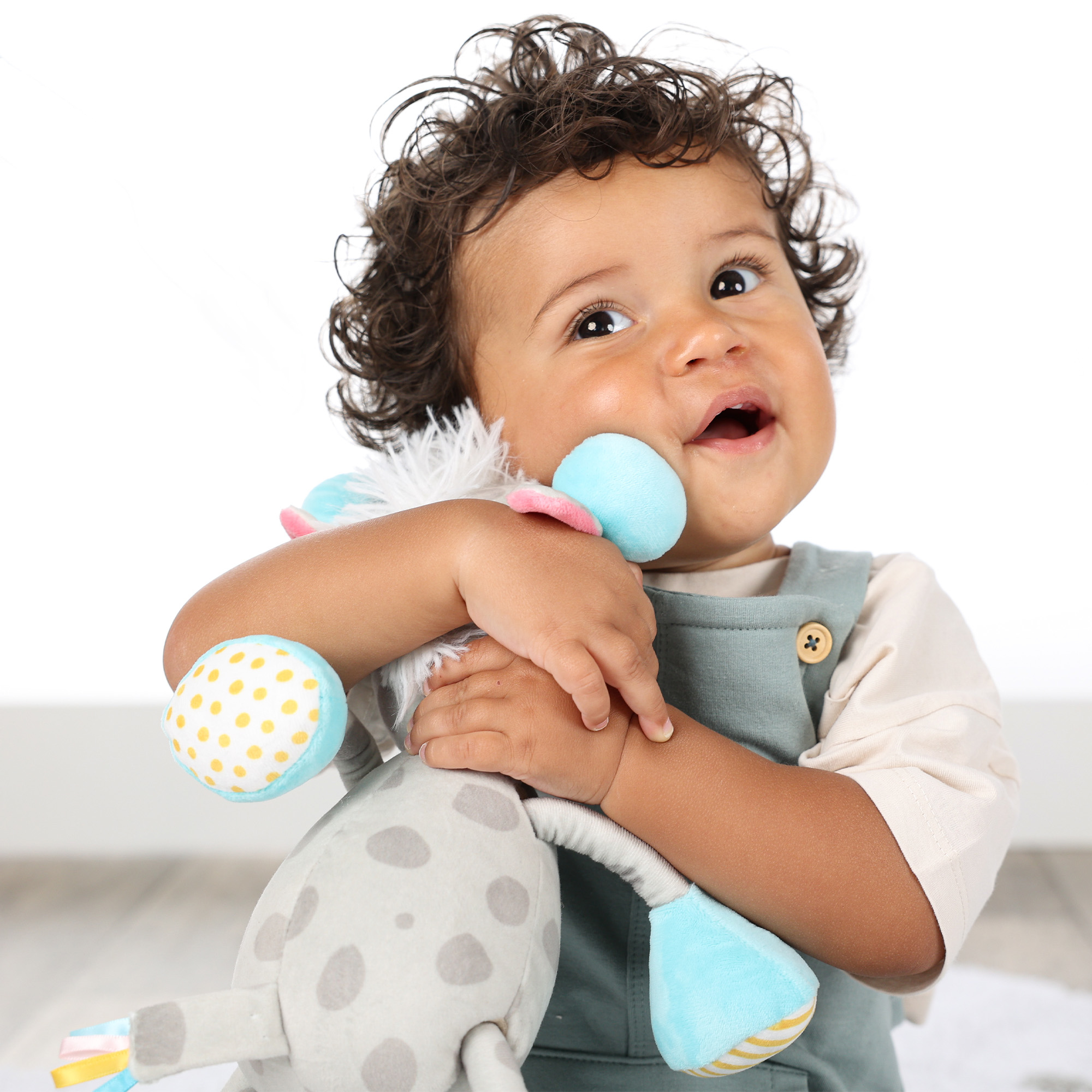 Ein Baby, das ein Stoffgiraffe hält, lächelt und nach oben schaut.