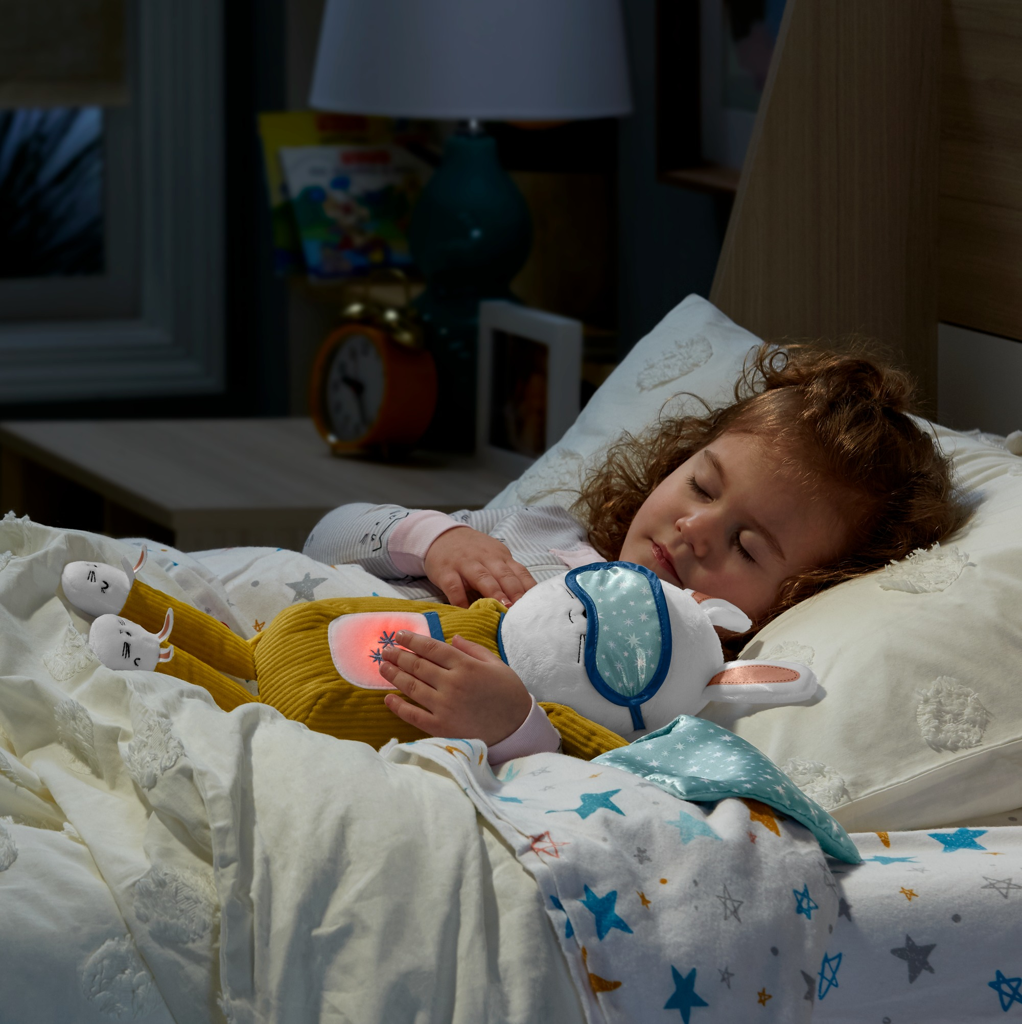Ein schlafendes Kind hält ein Kuscheltier. Der Raum ist dunkel. Das Spielzeug ist ein Hase mit Licht am Bauch.
