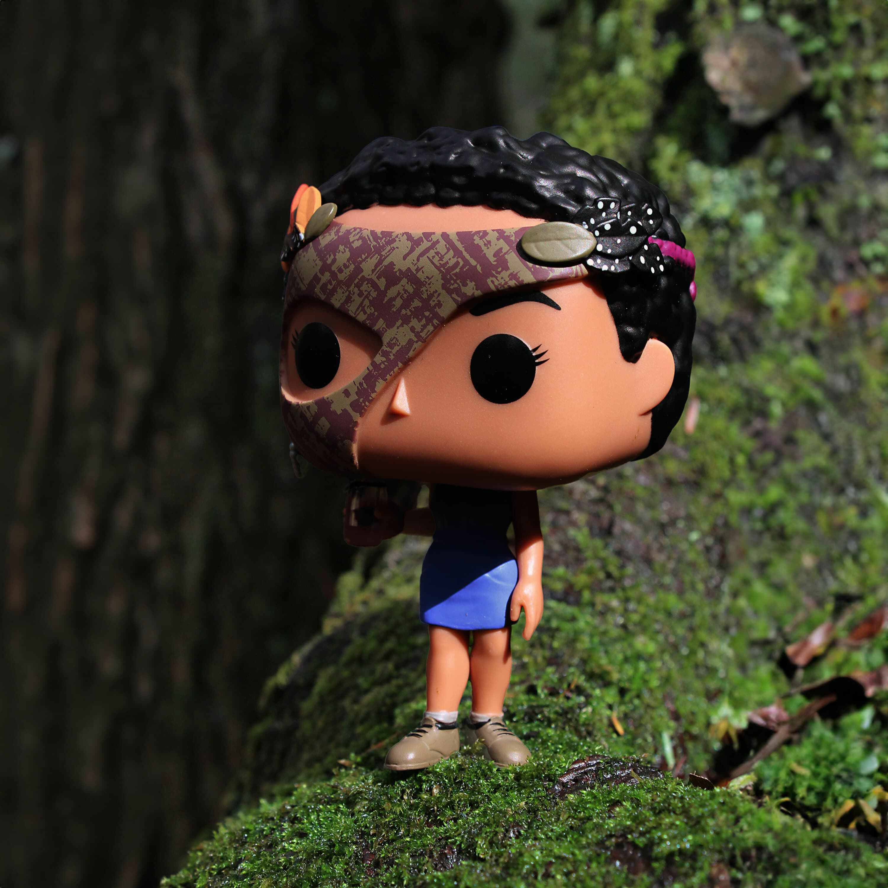 Figurka Funko Pop postaci z maską, stojąca na mszystym podłożu.