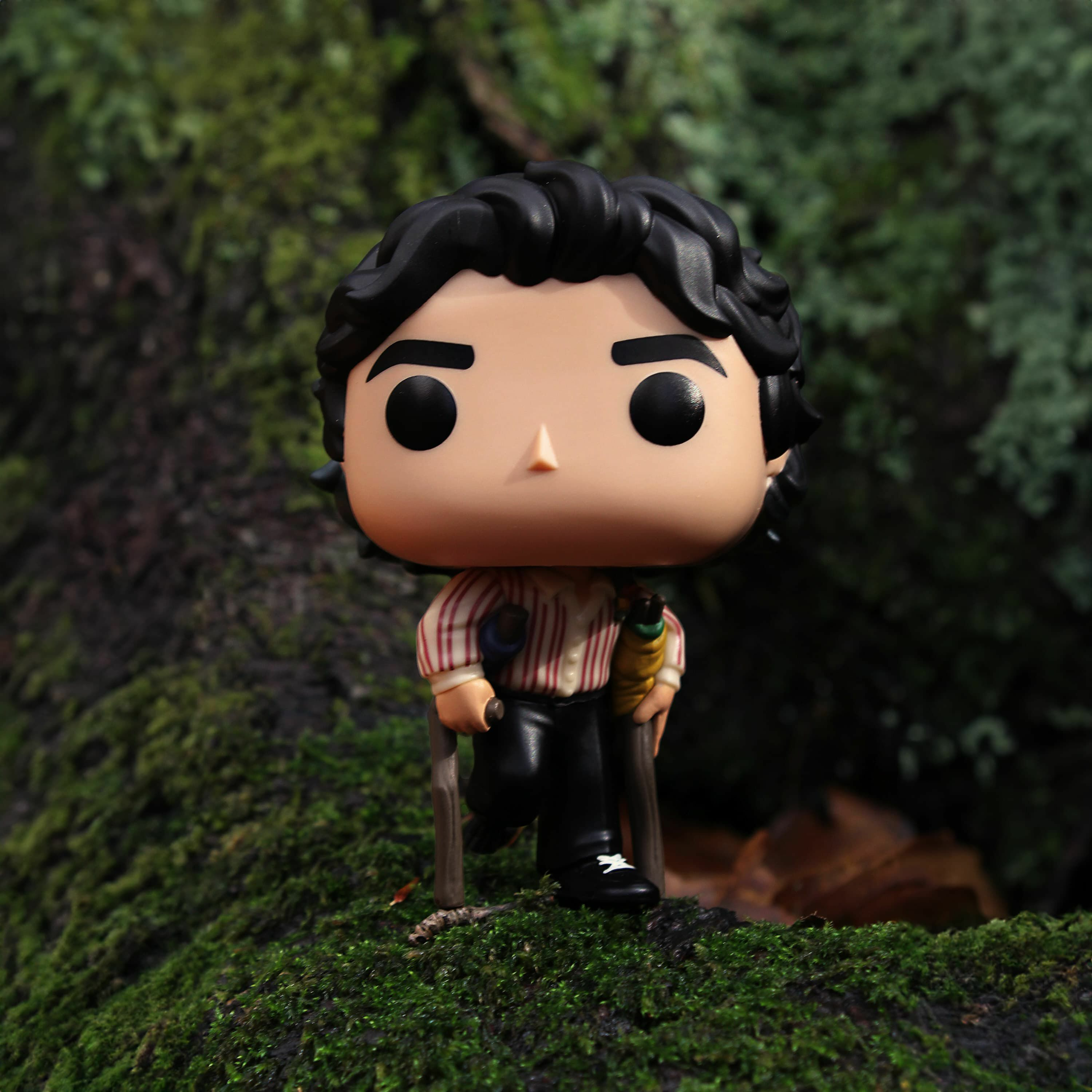 Figurka Funko Pop mężczyzny z ciemnymi włosami, trzymającego laskę. Stoi na mchu.