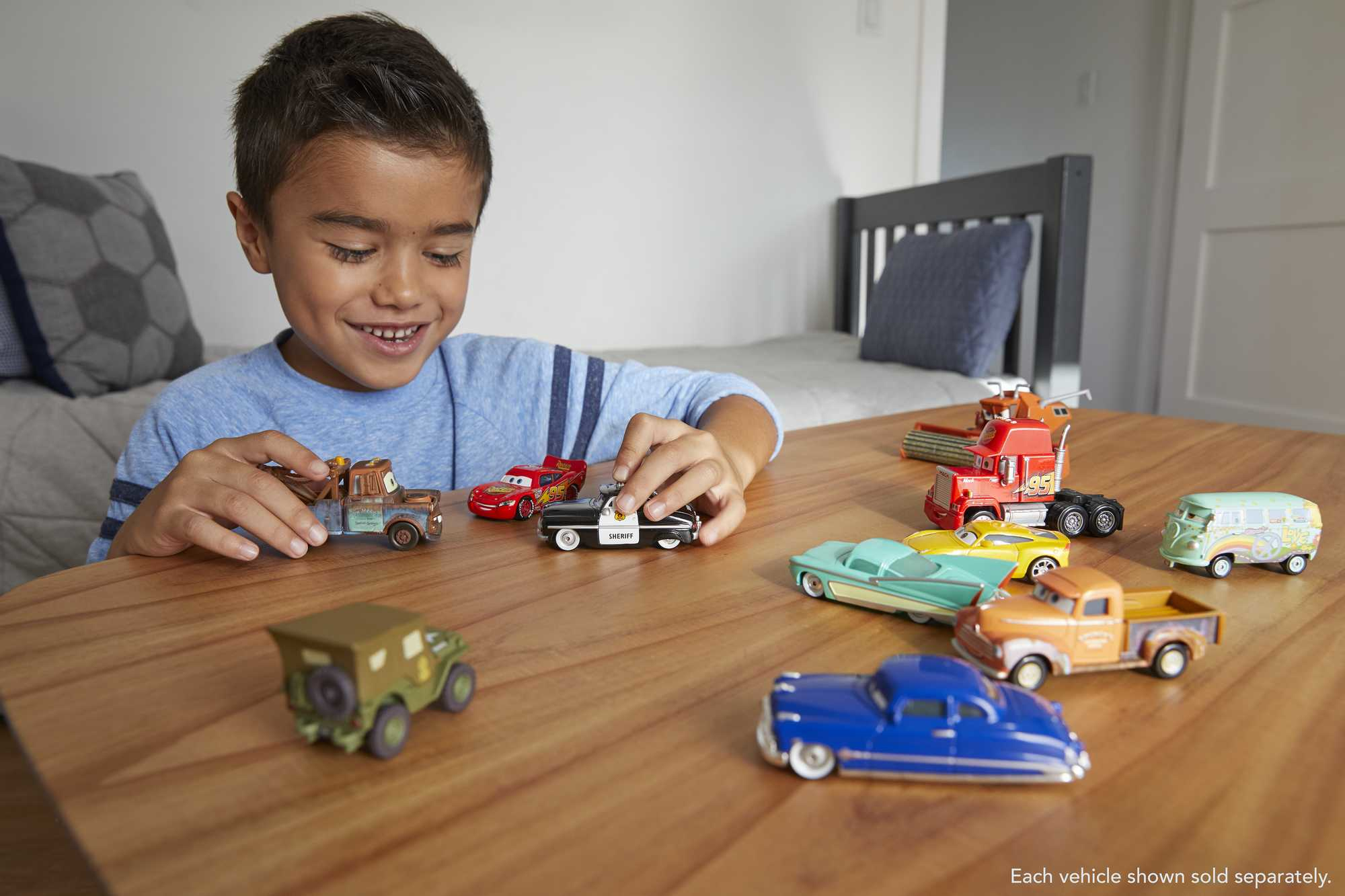 Un niño jugando con coches de juguete en una mesa. Los coches son de varios colores y estilos.