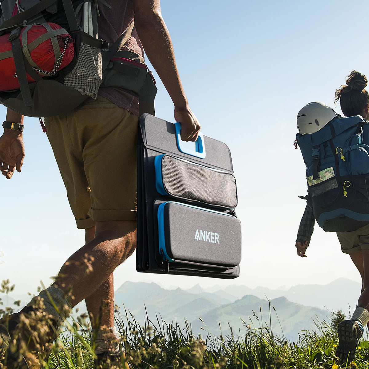 Zwei Personen wandern mit einem faltbaren Anker-Solarpanel. Einer trägt einen Rucksack. Sonnige Umgebung im Freien.