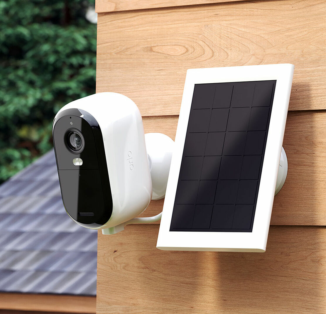 Eine weiße Überwachungskamera und ein Solarpanel sind an Holzverkleidungen montiert. Die Kamera hat ein schwarzes Objektiv.