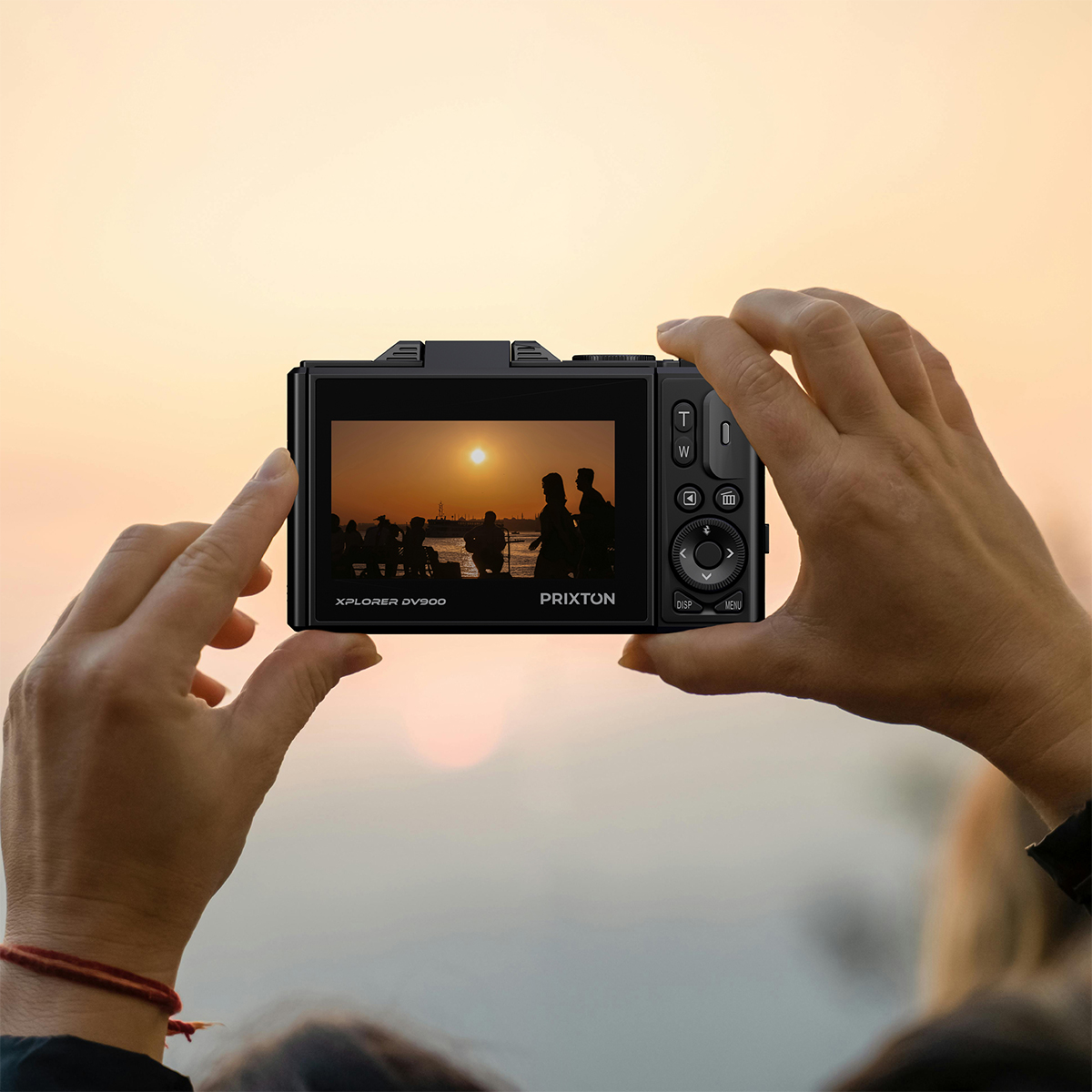 Ręce trzymające aparat, rejestrujące zachód słońca z sylwetkami.