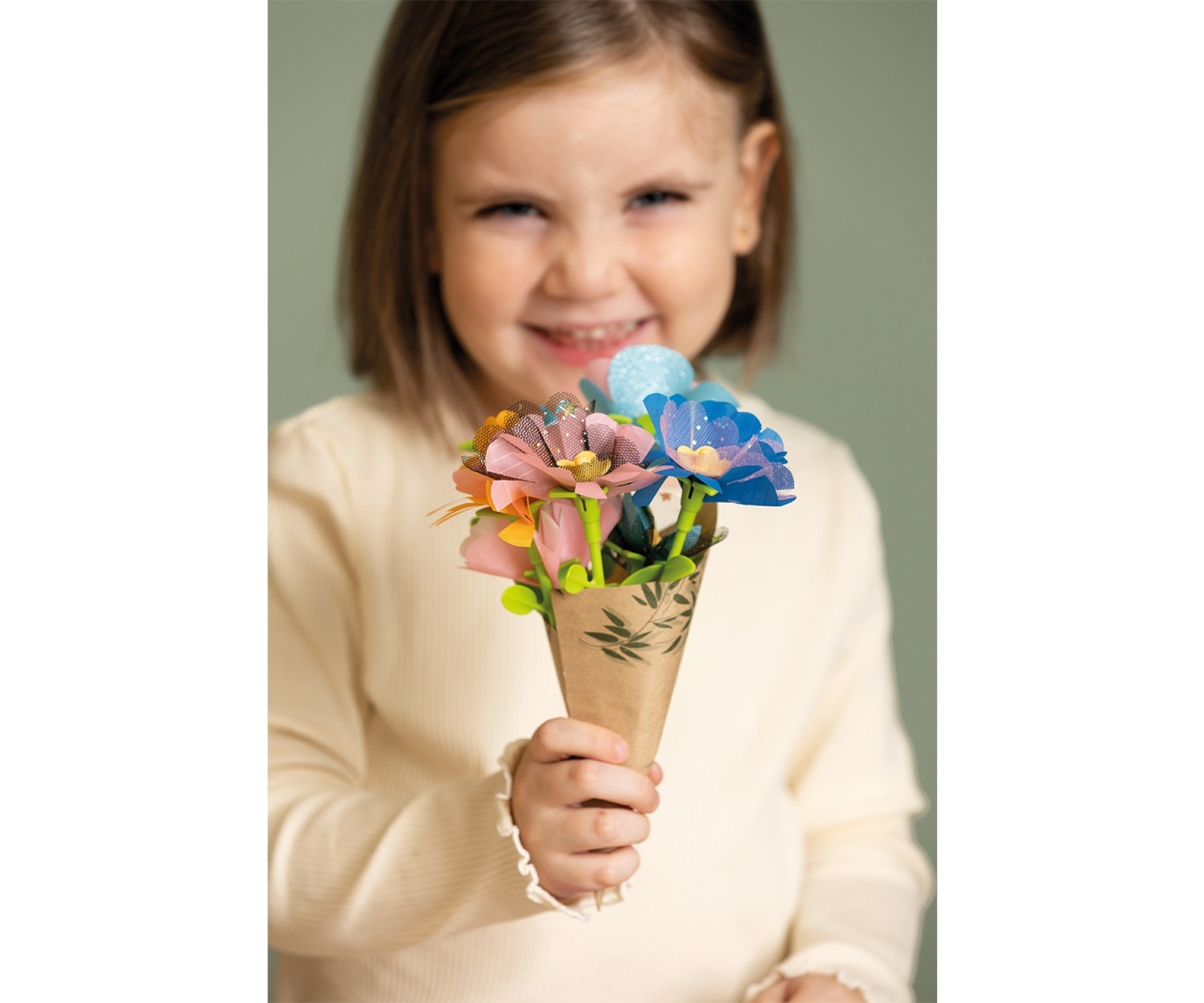 Ein Mädchen hält einen Kegel aus bunten Papierblumen und lächelt in die Kamera.