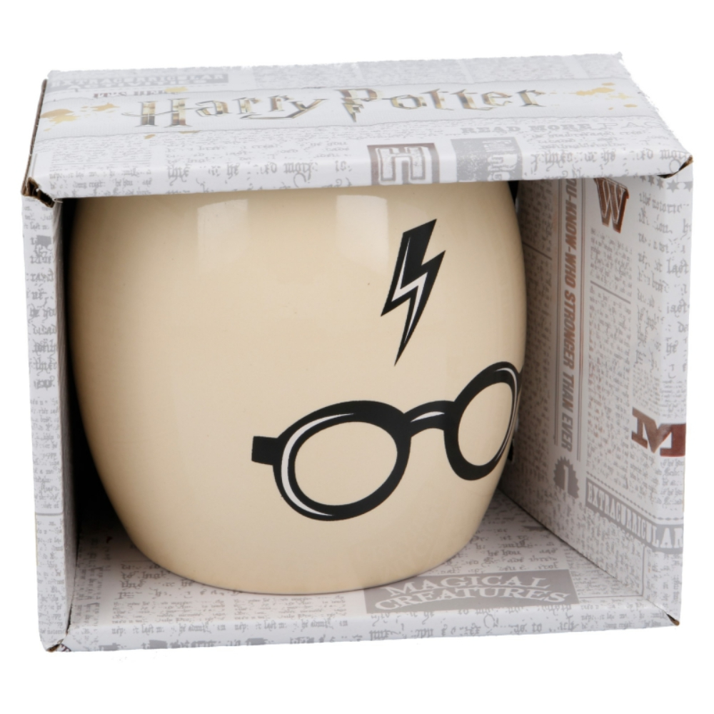 Una taza de Harry Potter en una caja. La taza tiene un rayo y gafas sobre fondo crema.