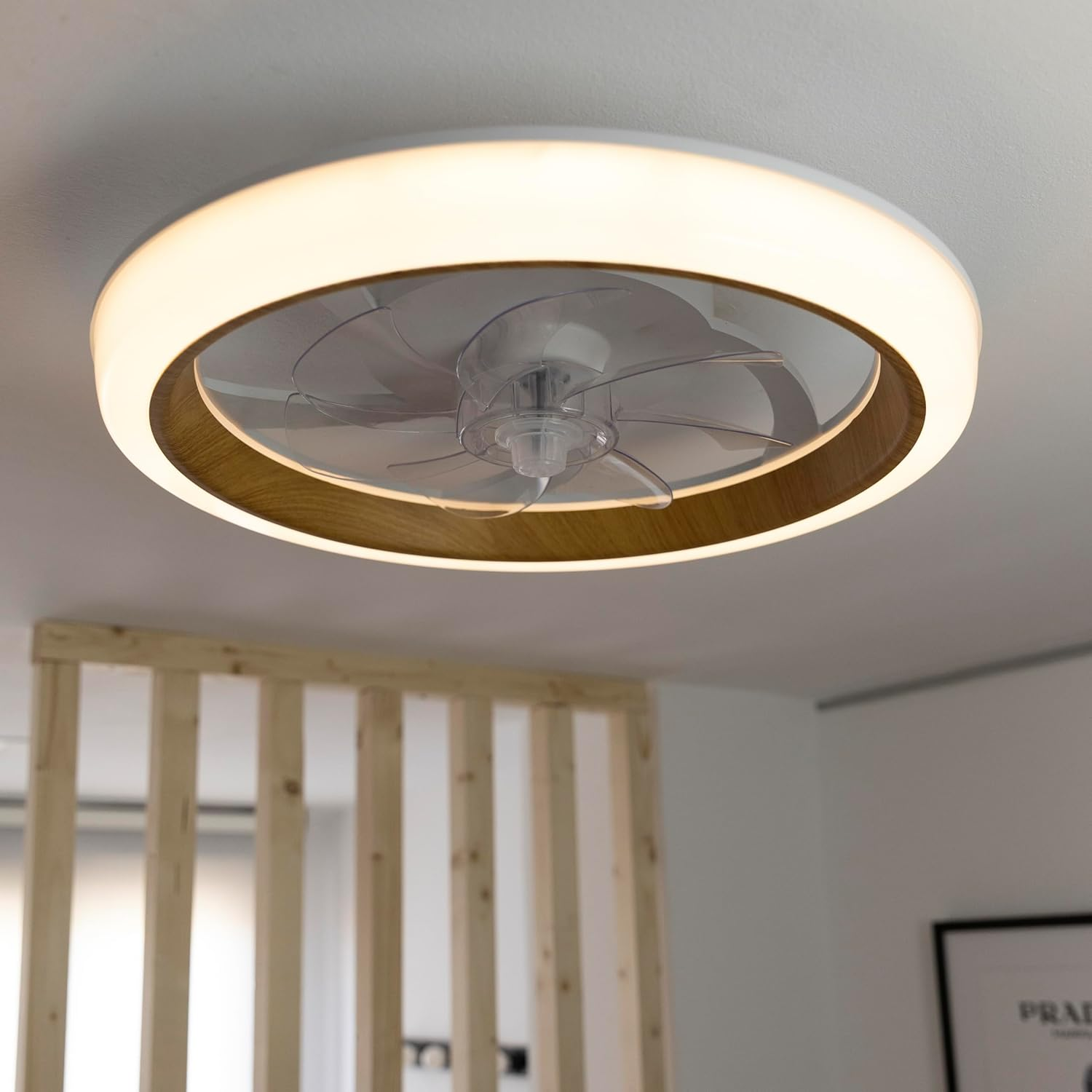 Ventilador de techo con un anillo de madera alrededor de la luz. Las aspas son transparentes.