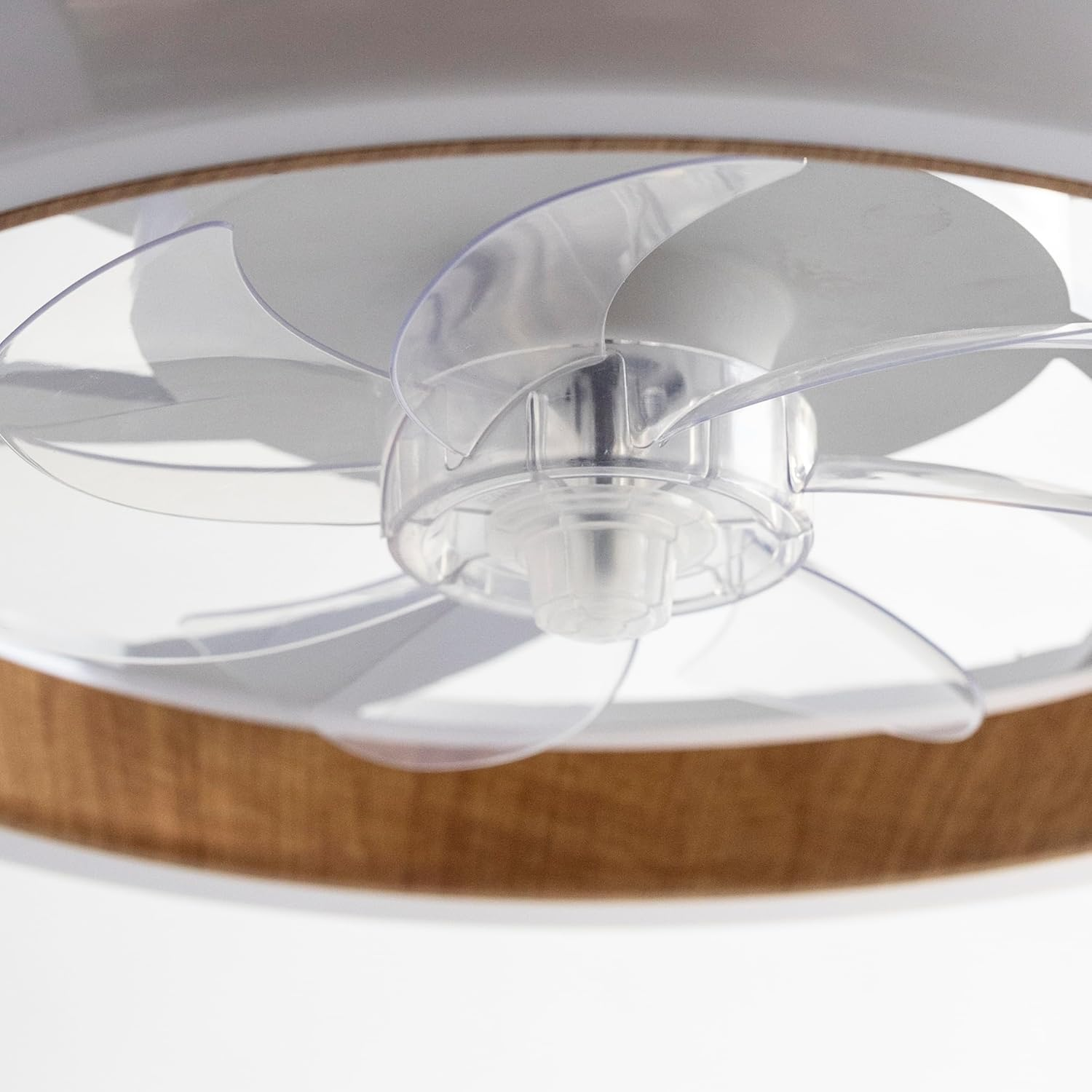 Ventilador de techo con aspas transparentes y un marco de madera marrón. Las aspas están anguladas y capturan la luz.