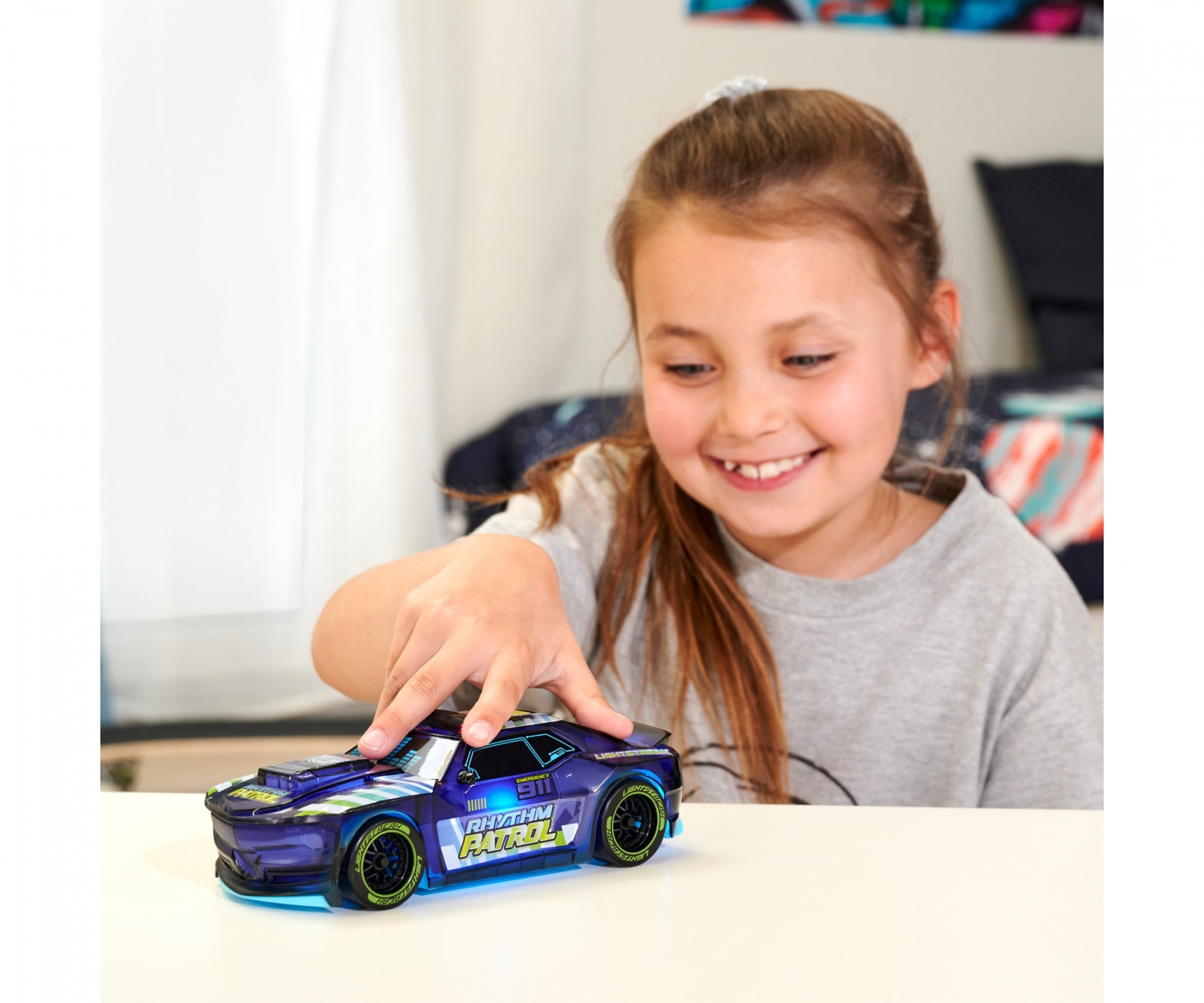 Dziewczyna uśmiecha się do zabawkowego samochodu z migającymi światłami na białym stole.