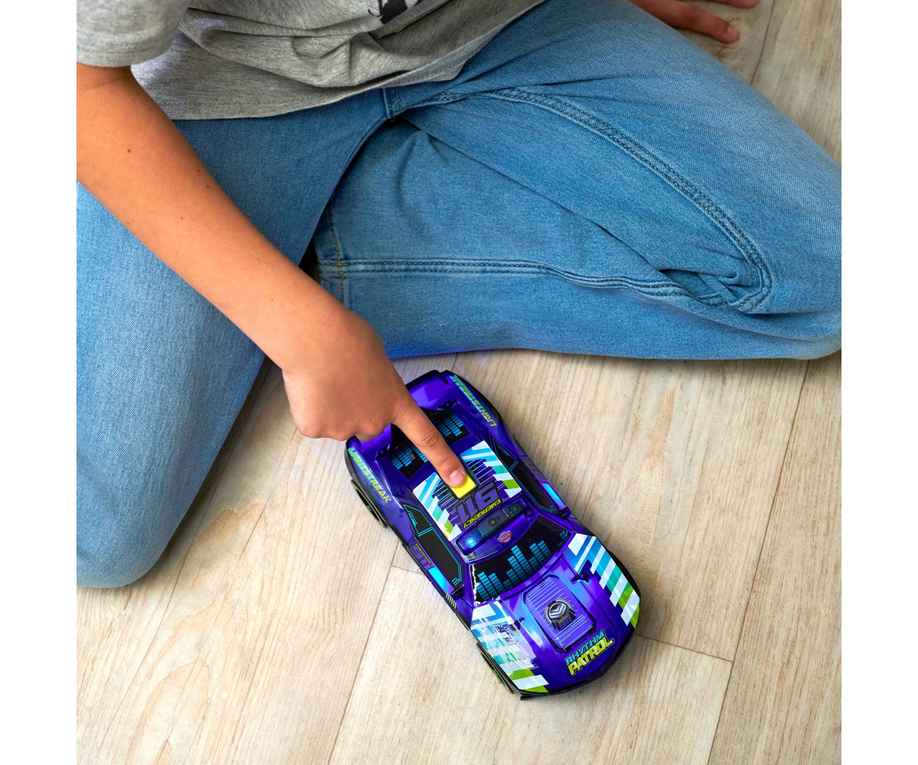 Ręka dziecka wskazująca na fioletowy samochodzik na podłodze. Samochód ma kolorowy design.