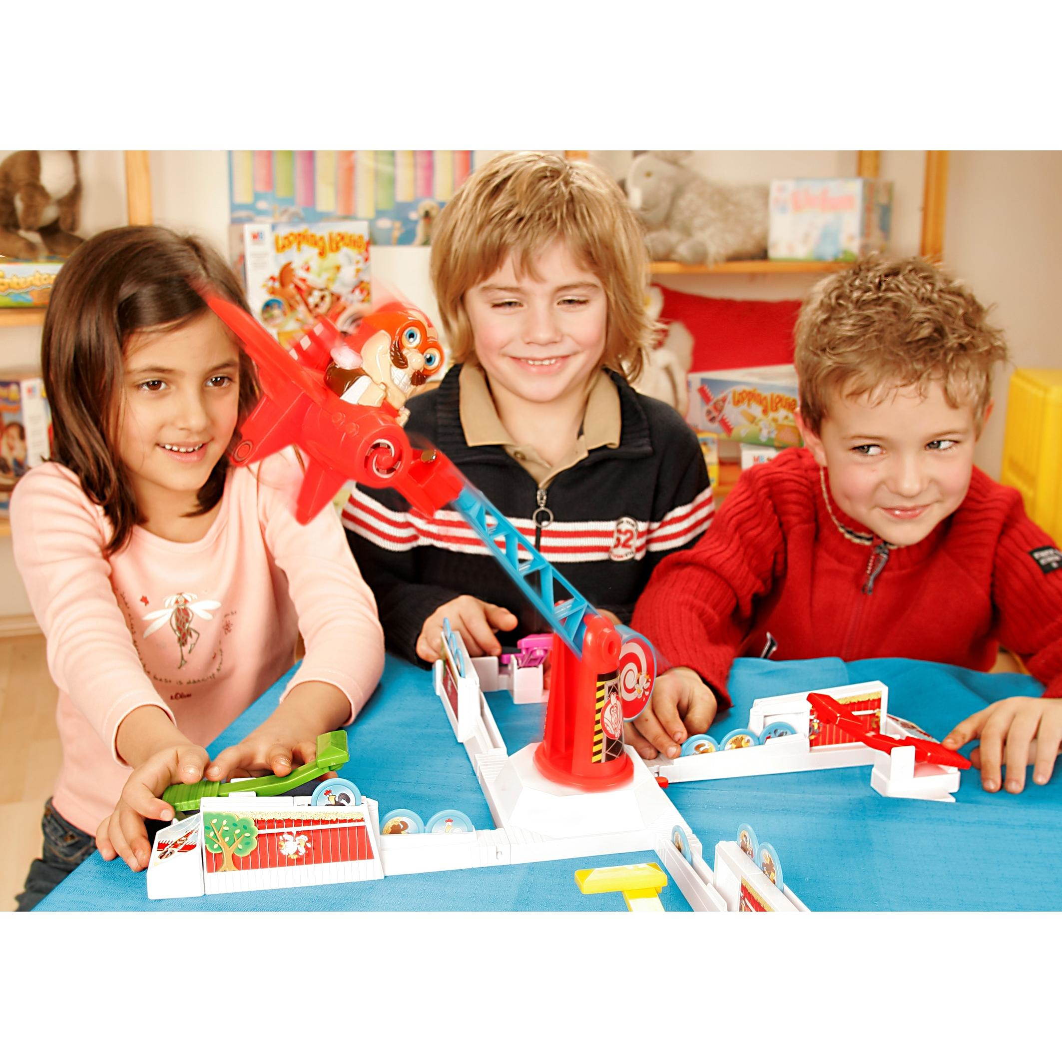 Drei Kinder spielen ein Spiel. Ein rotes Spielzeug mit einer Rakete, ein Tisch und zwei weitere Spielzeuge sind sichtbar.