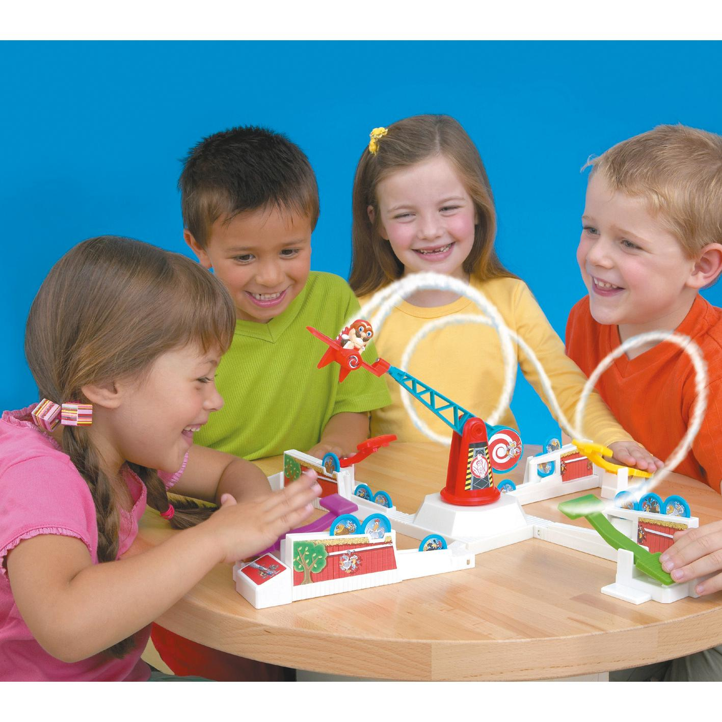 Vier Kinder spielen ein Spiel mit einem Spielzeug, das einen Affen startet. Sie lächeln und sind aufgeregt.