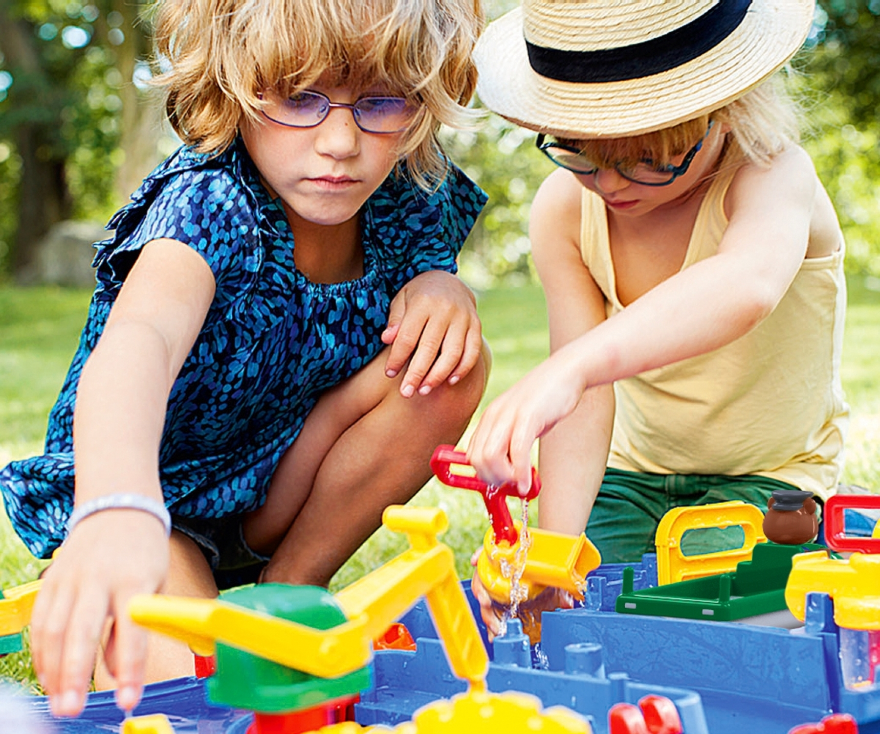 Zwei Kinder spielen an einem sonnigen Tag mit einem Wassertisch mit Spielzeug.