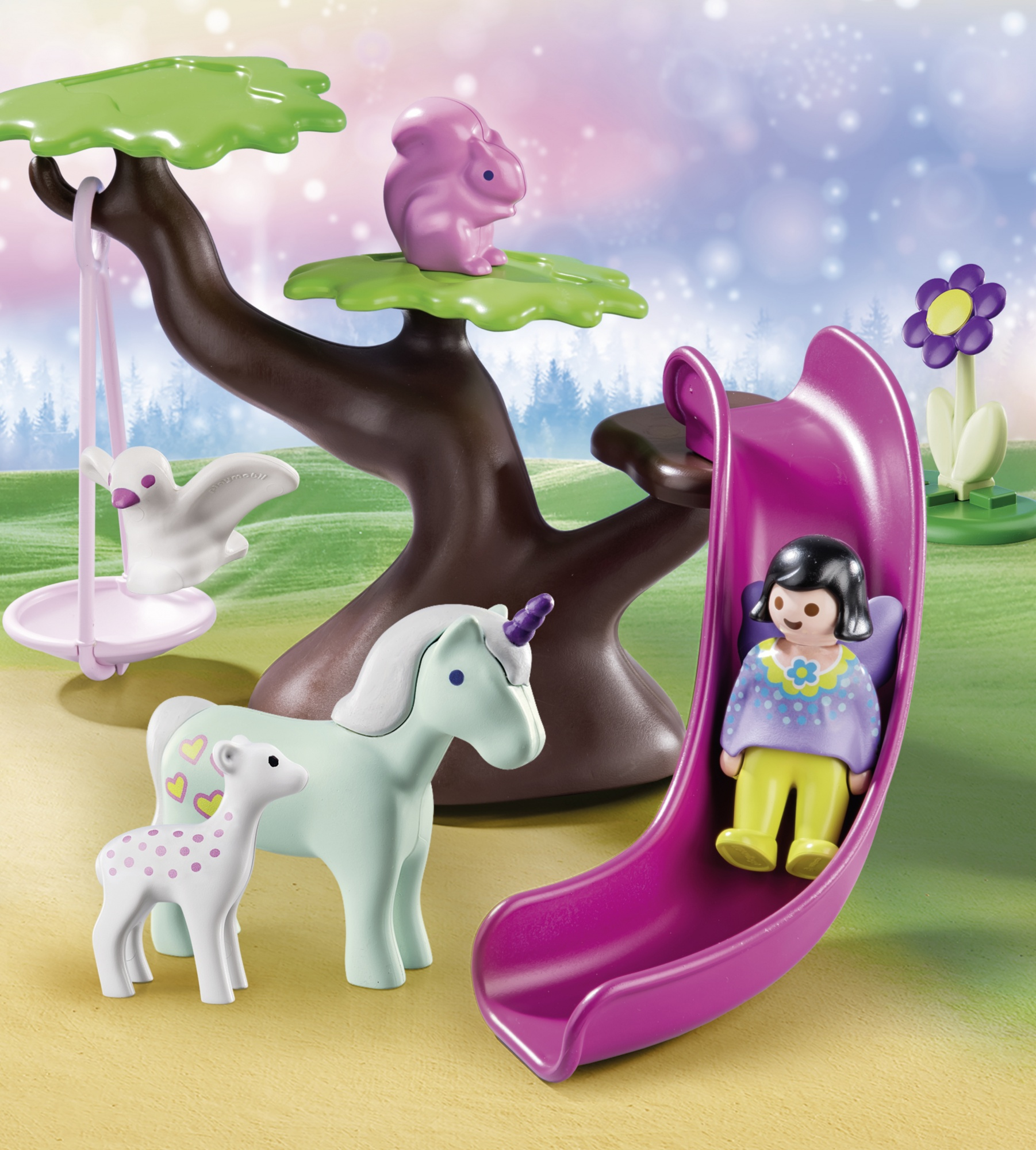Un playset Playmobil con un albero, uno scivolo e delle figure. Un unicorno e un agnello sono vicino all'albero.