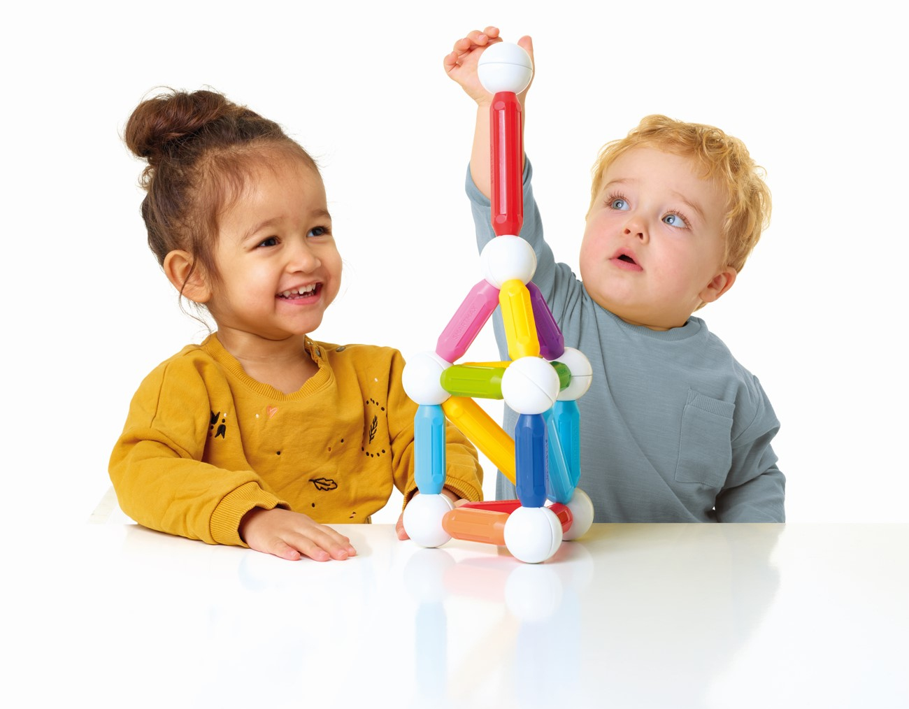 Deux enfants jouent avec un jouet de blocs de construction colorés. L'un sourit, l'autre regarde en haut.