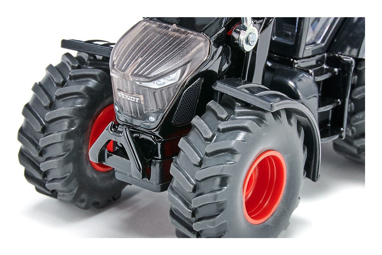 Zbliżenie czarnego traktora zabawki, z czerwonymi kołami i częściowo widocznym grillem.