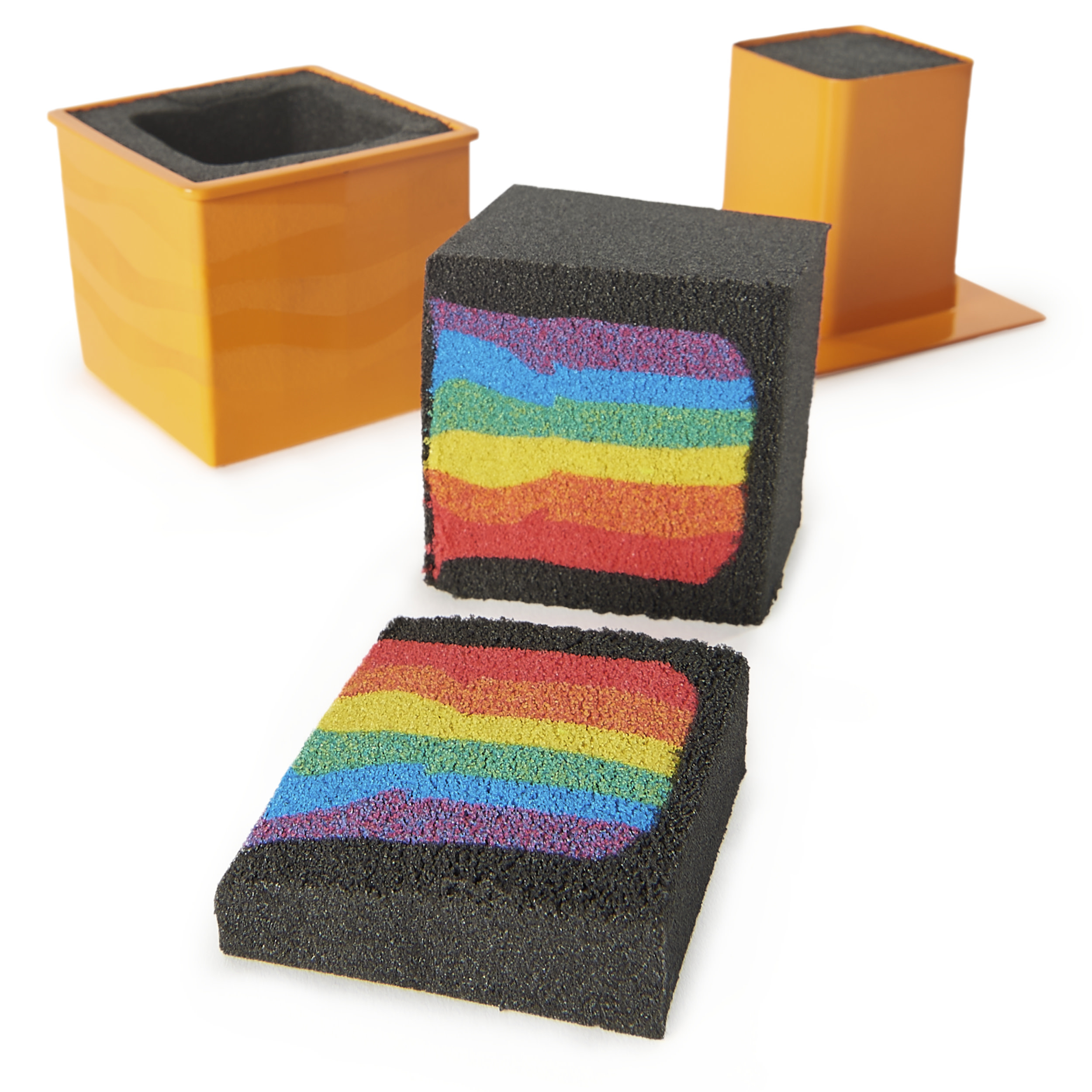 Un bloc de mousse noir en couches arc-en-ciel, coupé en deux morceaux, avec deux contenants orange en arrière-plan.