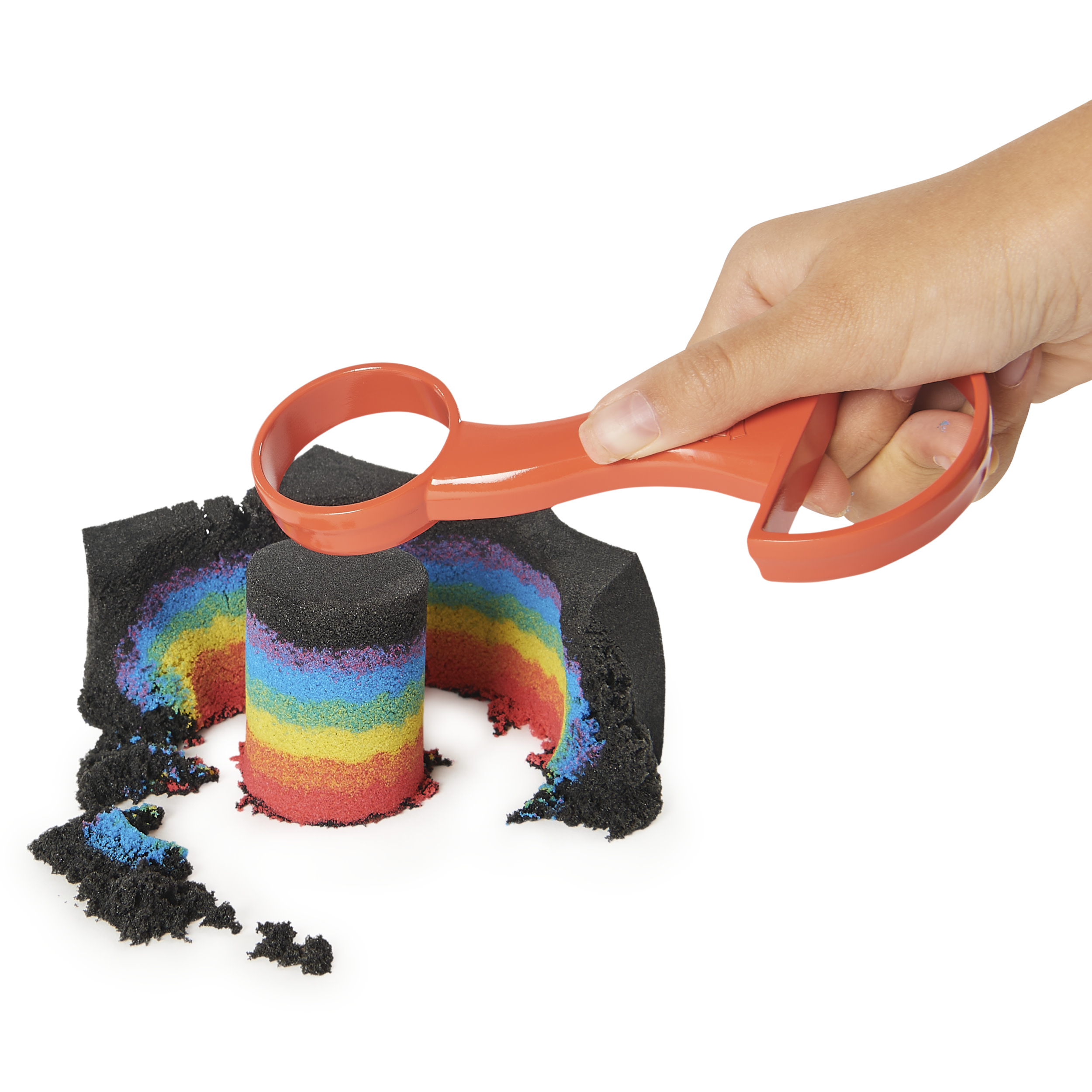 Une main tient un outil rouge coupant à travers une œuvre d'art en sable colorée avec des couches arc-en-ciel.