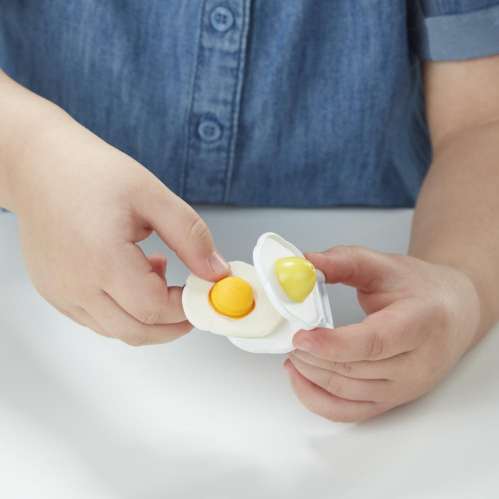 Kinderhände halten ein Spielzeugei mit gelbem Eigelb. Weißer Tischhintergrund.