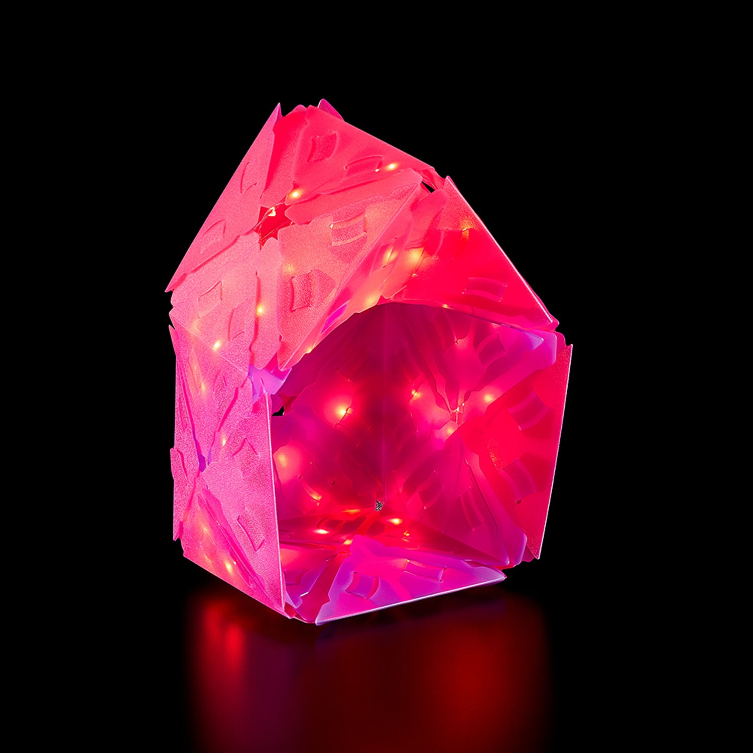 Rosa beleuchtetes Origami-Haus, schwarzer Hintergrund. Innenlichter sind sichtbar.