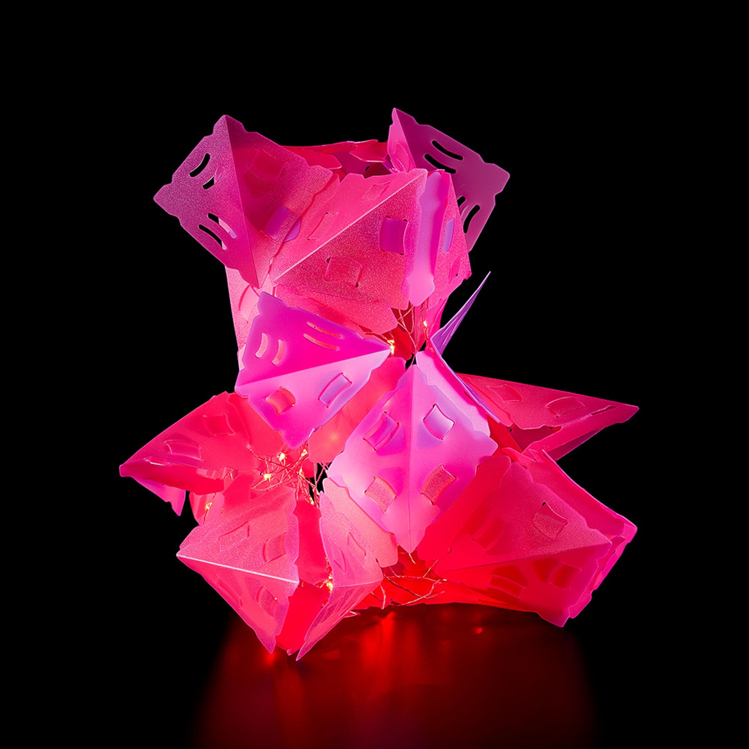 Eine rosa, geometrische, beleuchtete Skulptur auf schwarzem Hintergrund.