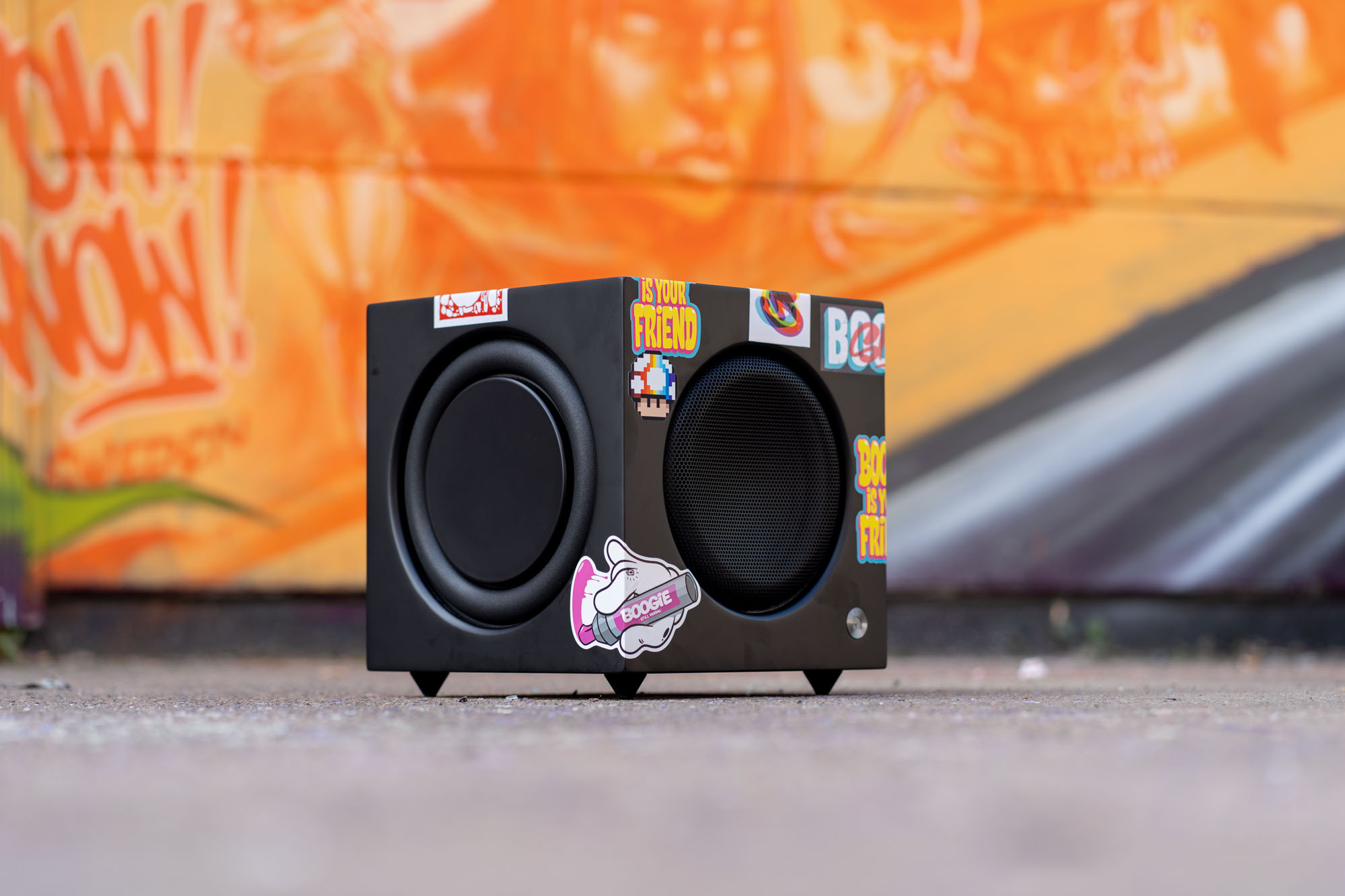 Haut-parleur noir avec autocollants sur béton. Graffiti orange et blanc en arrière-plan.