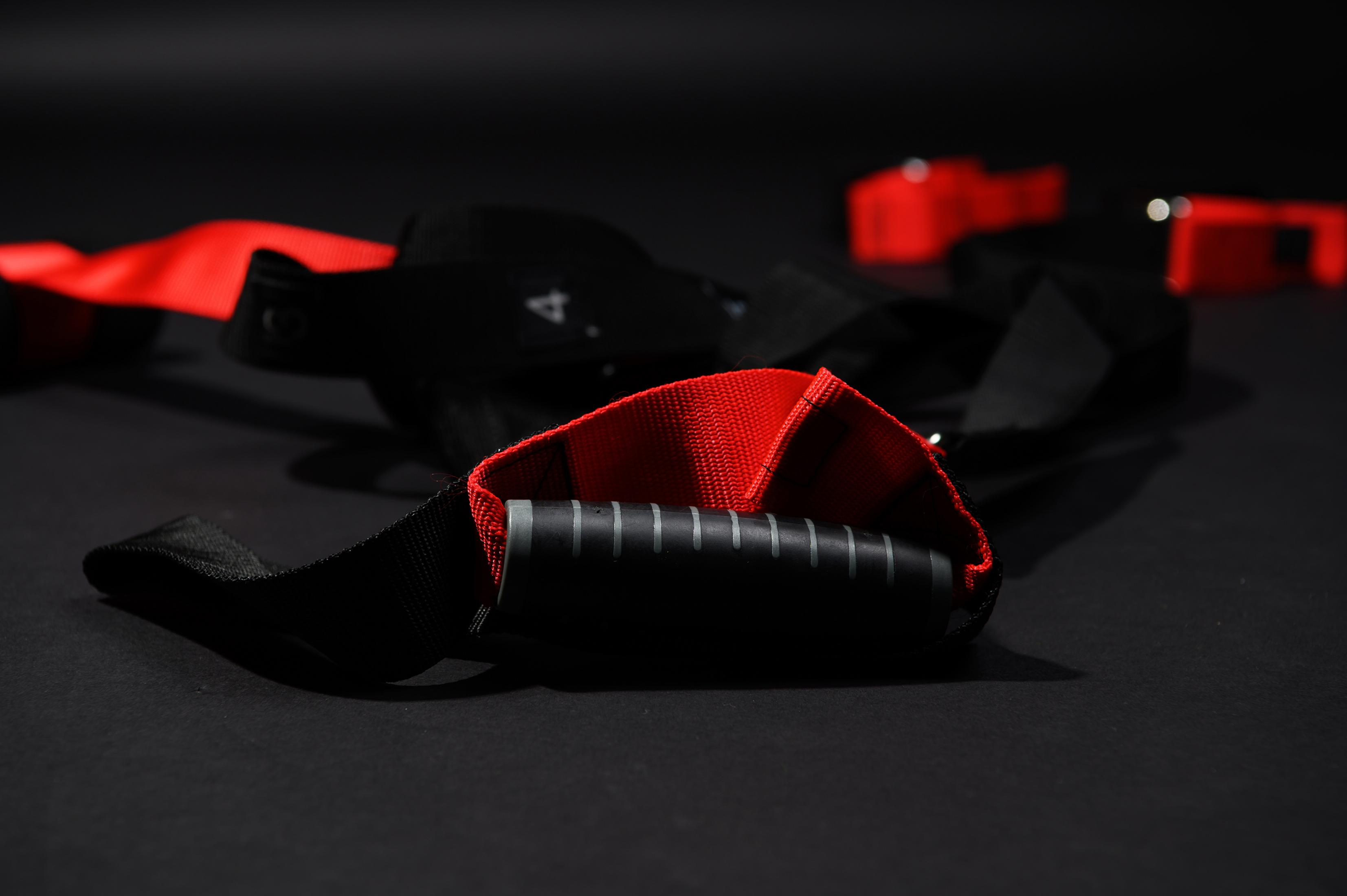 Schwarz-rote Trainingsgurte auf dunklem Hintergrund. Schwarze Griffe. Selektiver Fokus.