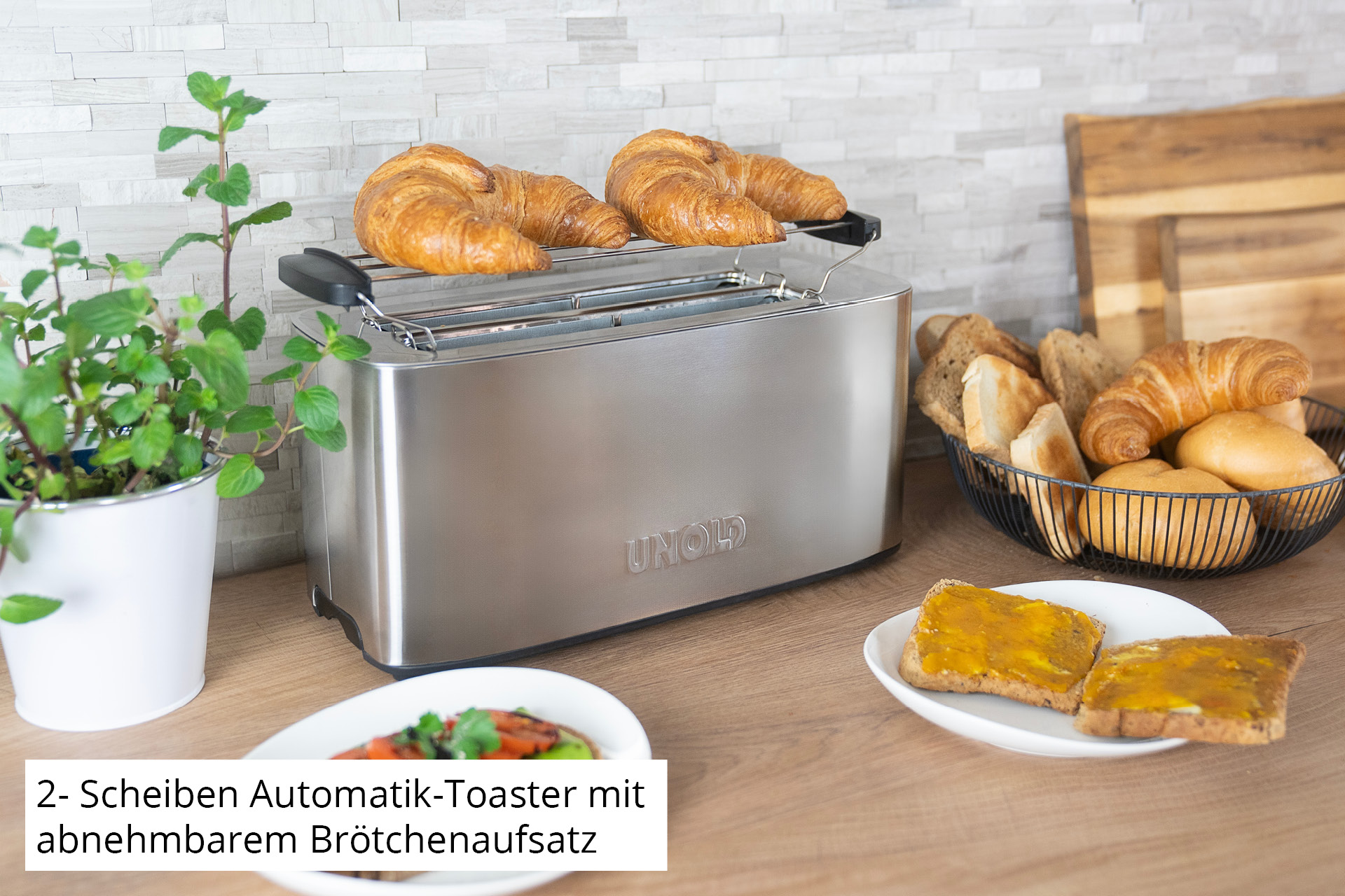 Ein Edelstahl-Toaster mit Croissants oben drauf und Toast auf dem Teller.