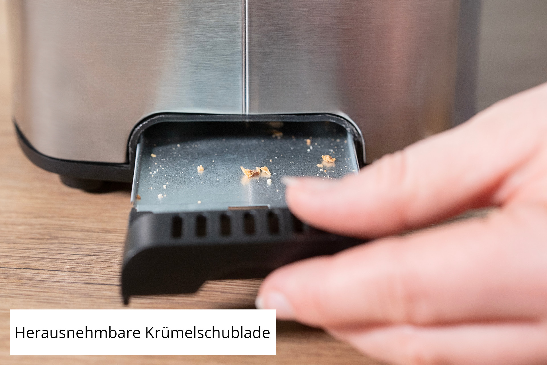 Krümelschublade des Toasters. Hand zieht die Schublade aus einem silbernen Toaster.