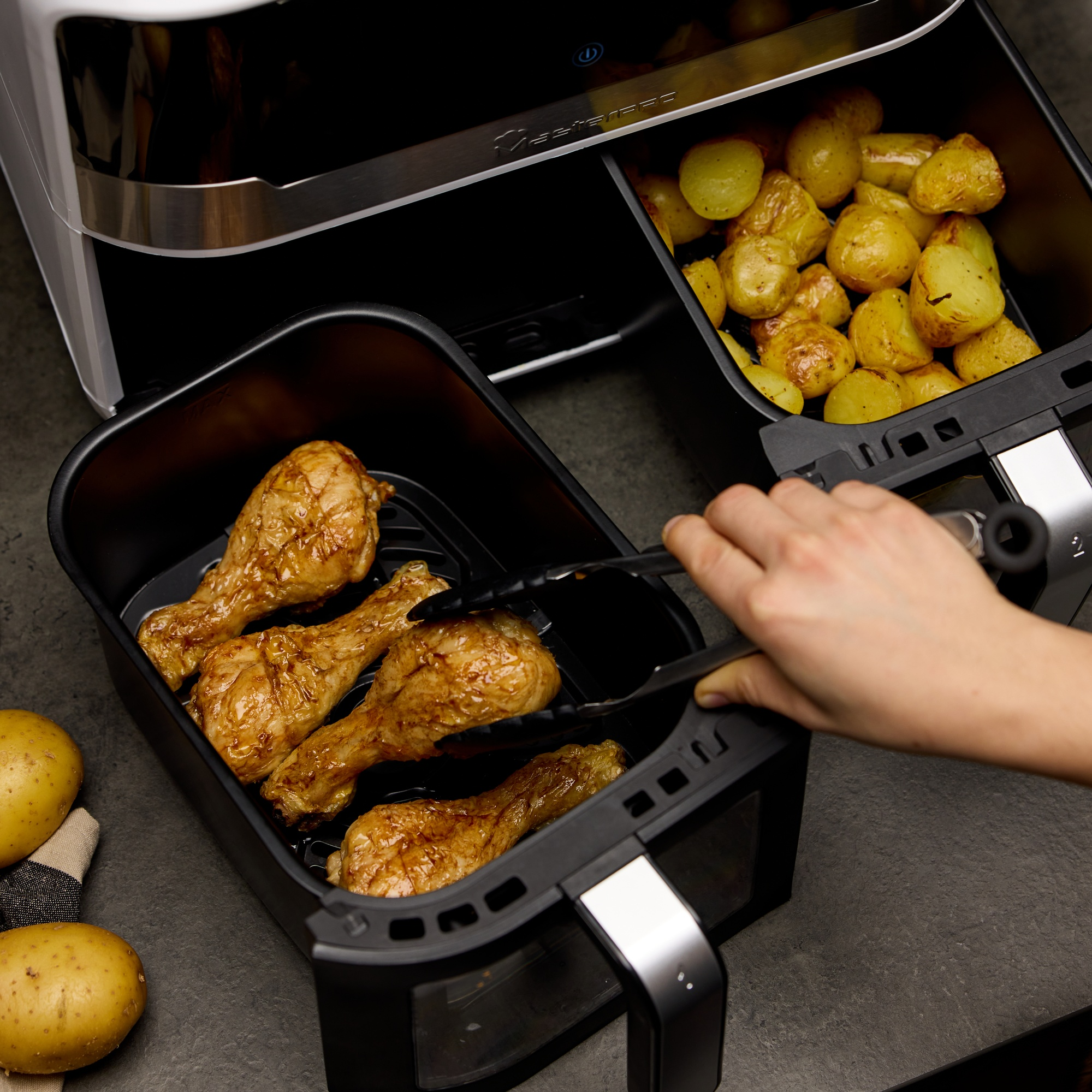 Friggitrice ad aria con cosce di pollo che vengono inserite all'interno. Le patate sono nell'altro cestello.