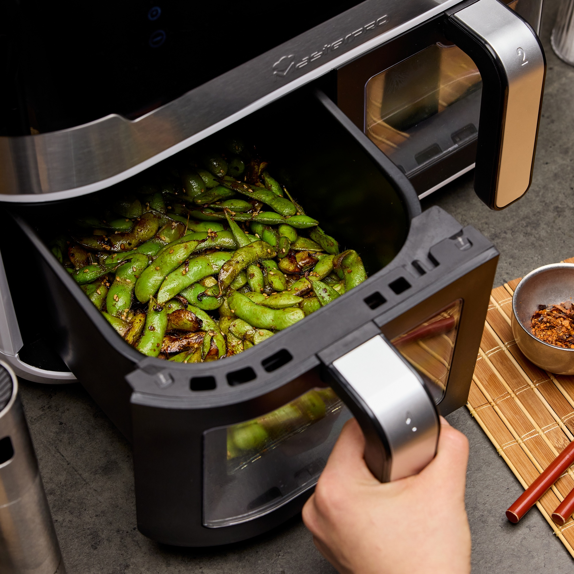 Friggitrice ad aria con edamame verde. Una mano tiene il vassoio.