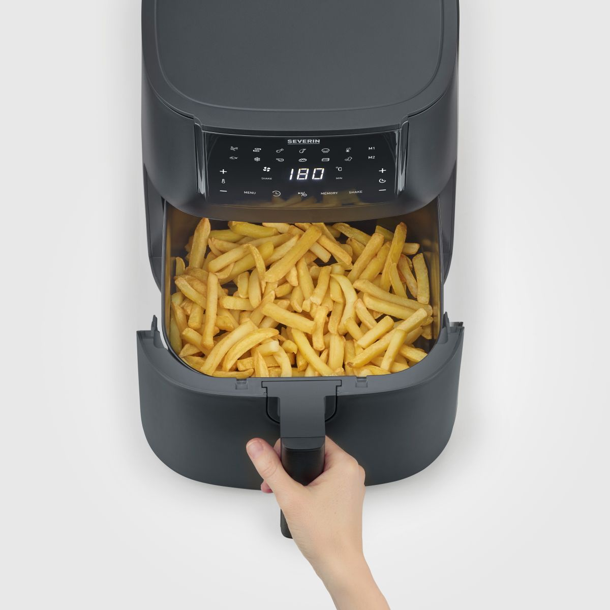 Een heteluchtfriteuse met de lade open, gevuld met friet. Een hand houdt de handgreep vast.