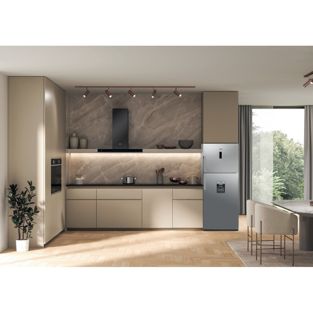 Cucina moderna con frigorifero argentato. Armadi beige, piano nero e luci visibili.