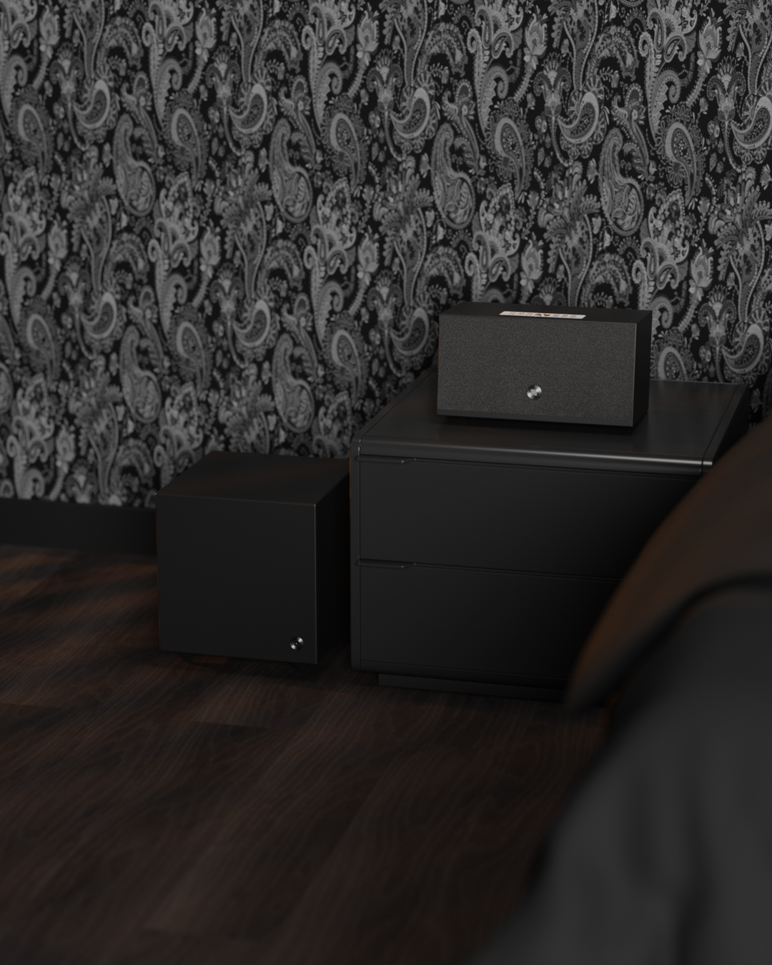Black nightstand with a speaker and a small side table against a paisley wallpaper.