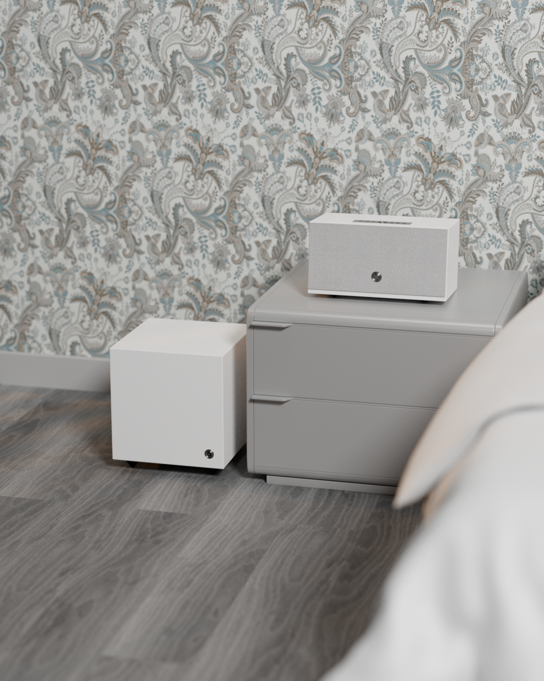 A white speaker on a gray nightstand next to a white cube and a patterned wallpaper.