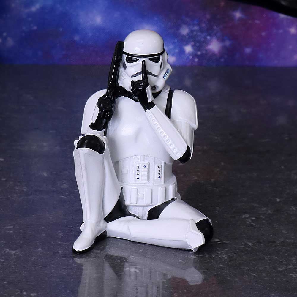 Wit Stormtrooper figuur in zittende pose, houdt een geweer vast, vinger op lippen. Donkere achtergrond.