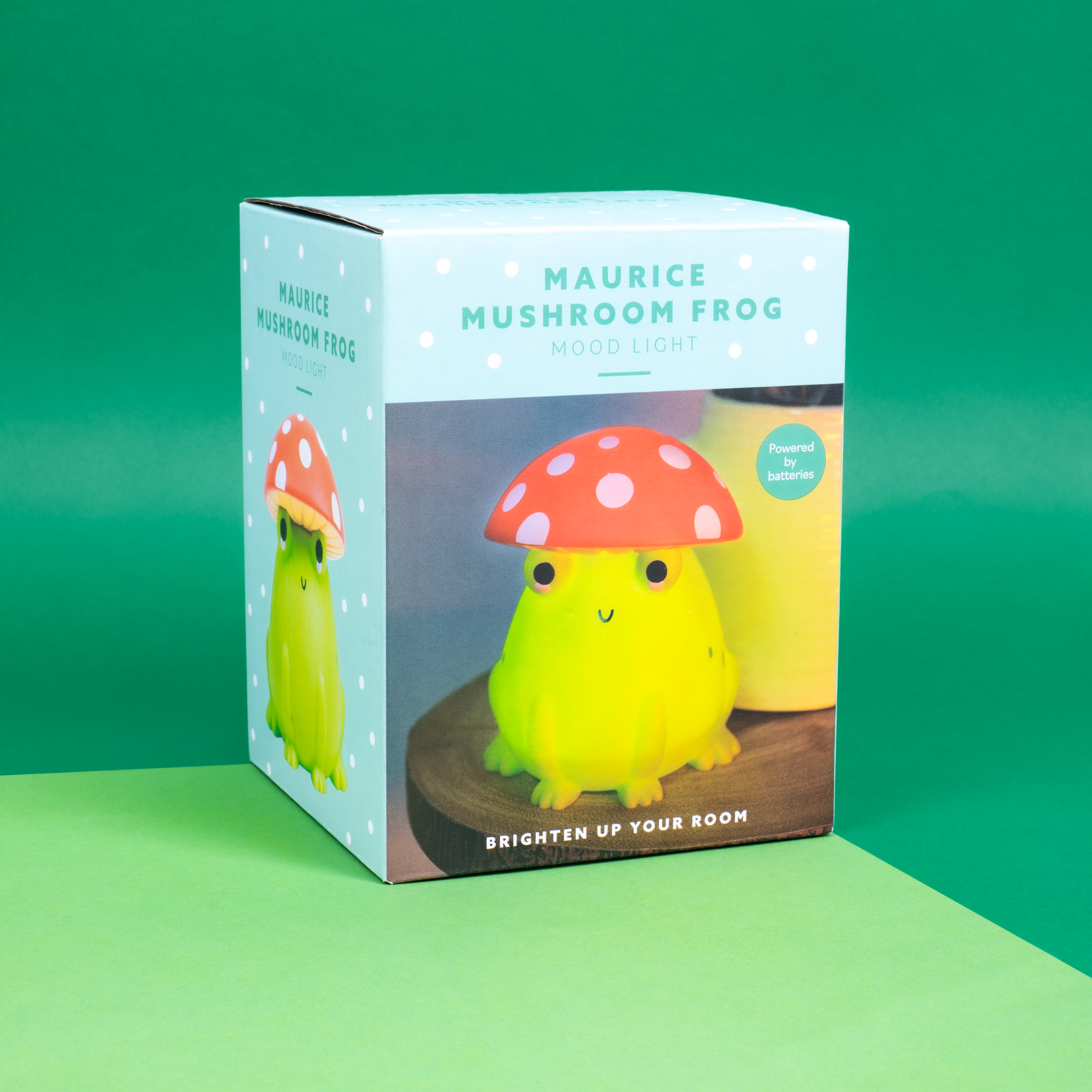 Kikker-vormige sfeerlamp in een doos. Groene kikker met oranje paddenstoel hoed. Doos zegt 'Maurice Mushroom Frog'.