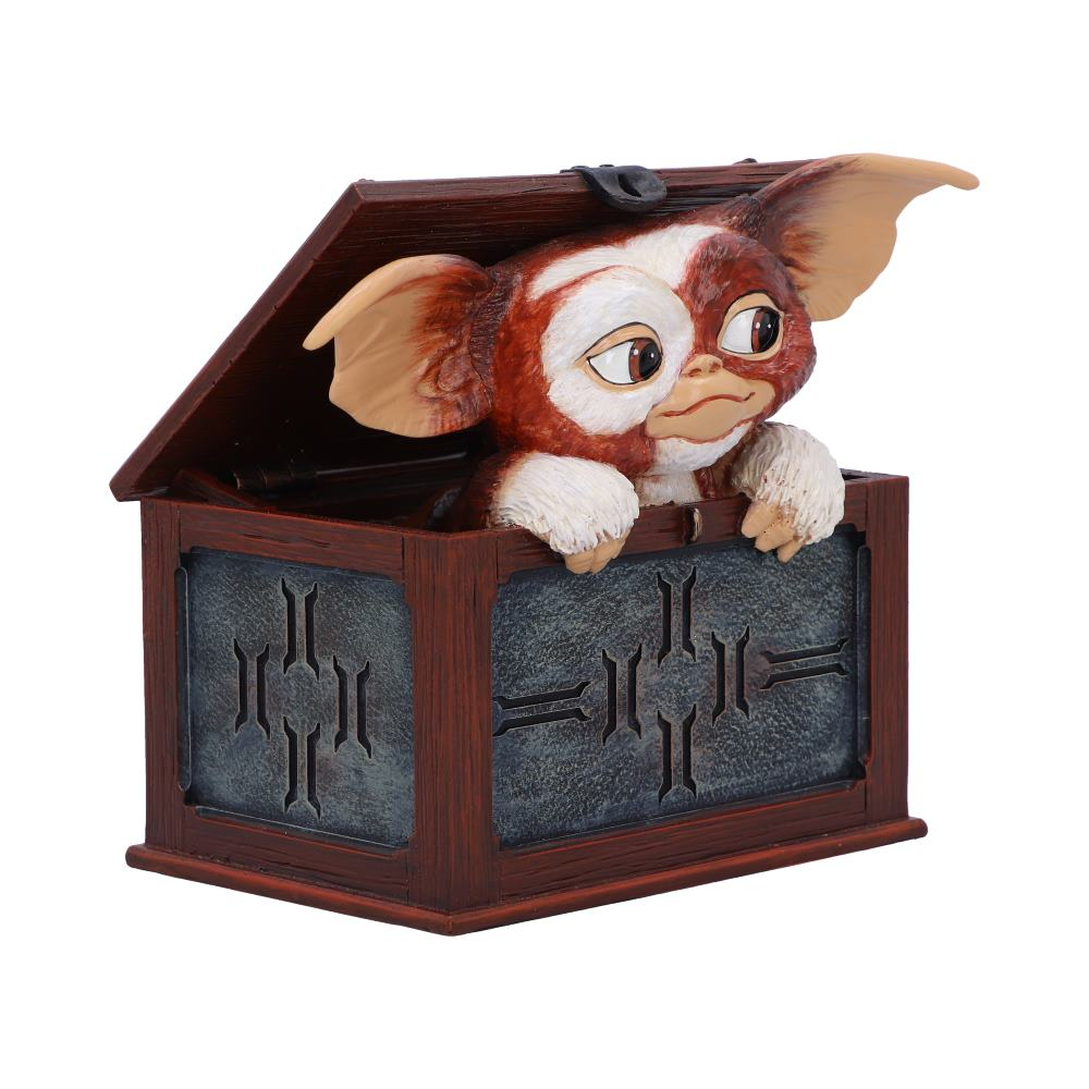 Gremlin-figuur in een houten kist. Gremlin is bruin en wit, kijkt naar buiten. Kist heeft een donker, metalen paneel.