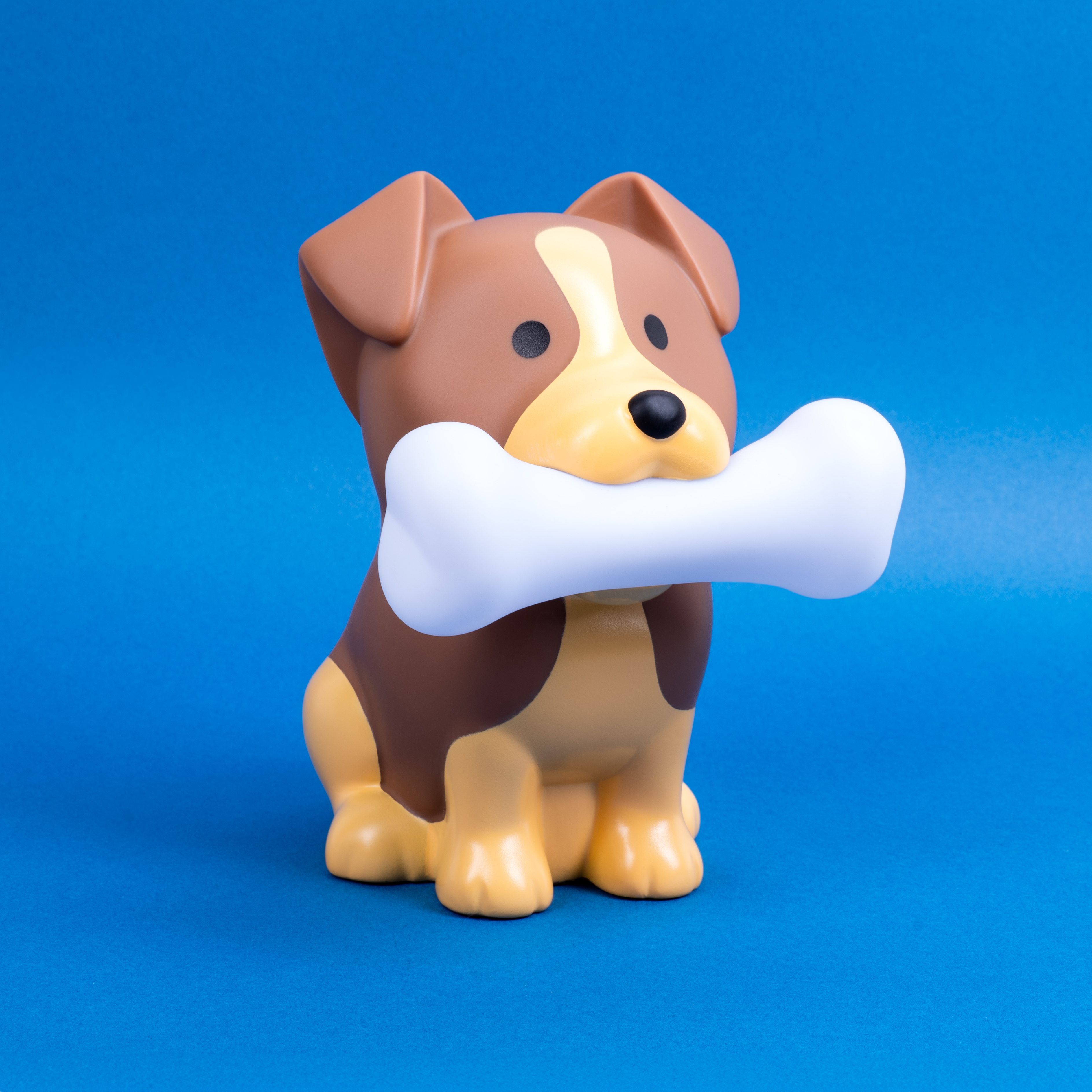 Dog figurine holding a bone. Brown and tan colors, blue background.