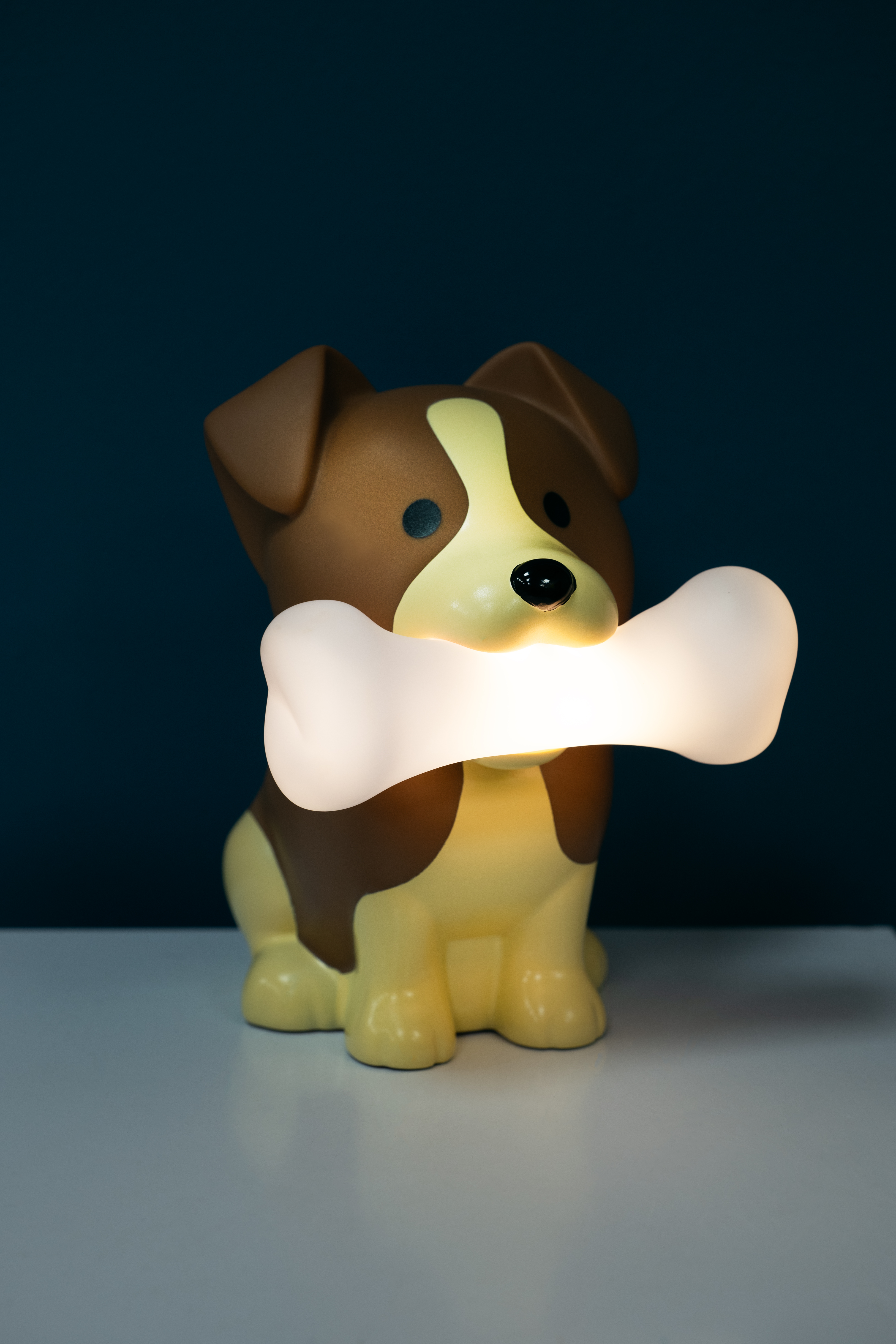 Dog lamp holding a bone-shaped light. Brown and yellow dog. Dark background.