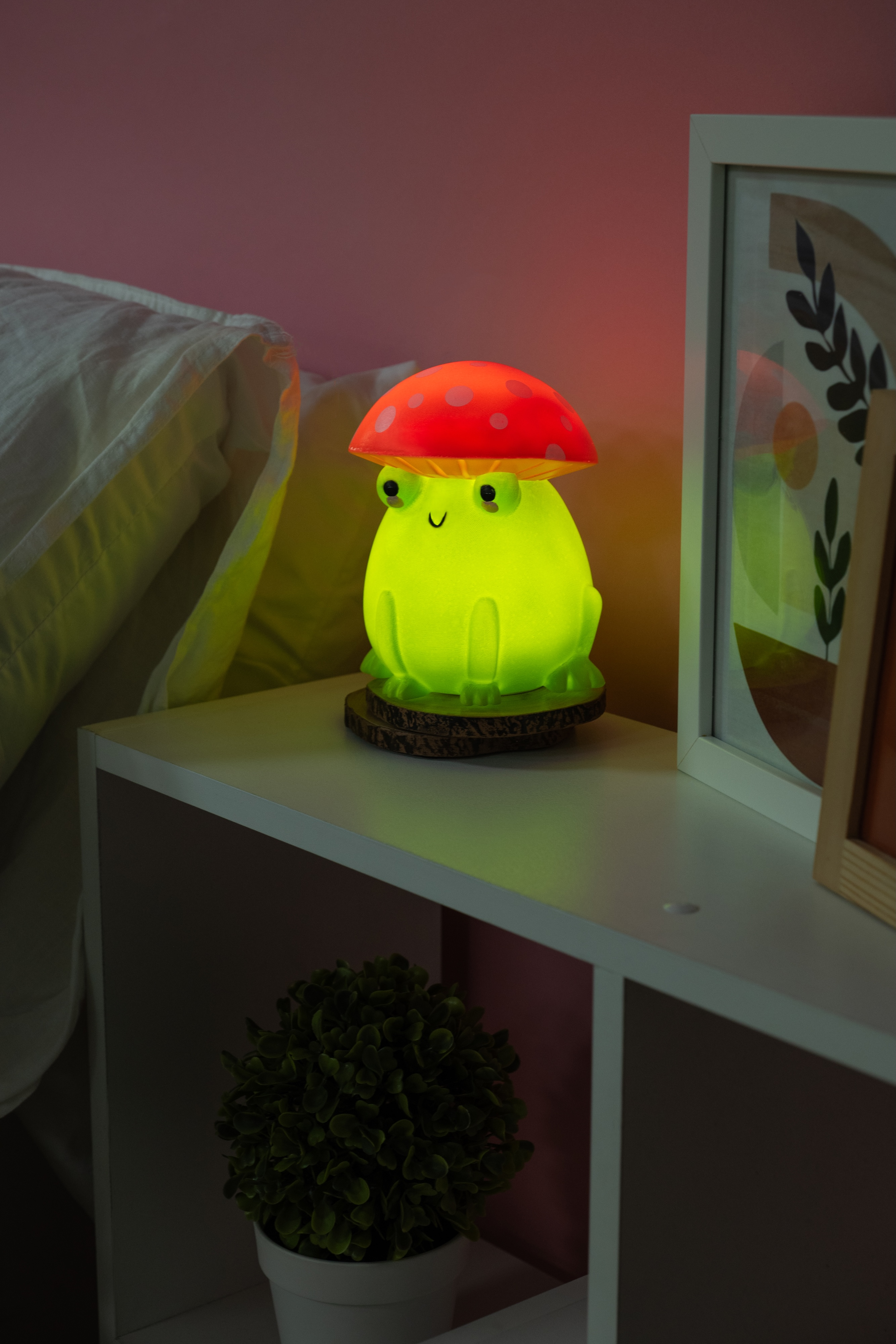 Kikkerlamp met paddenstoel, groene body, op houten voet, op een witte plank.