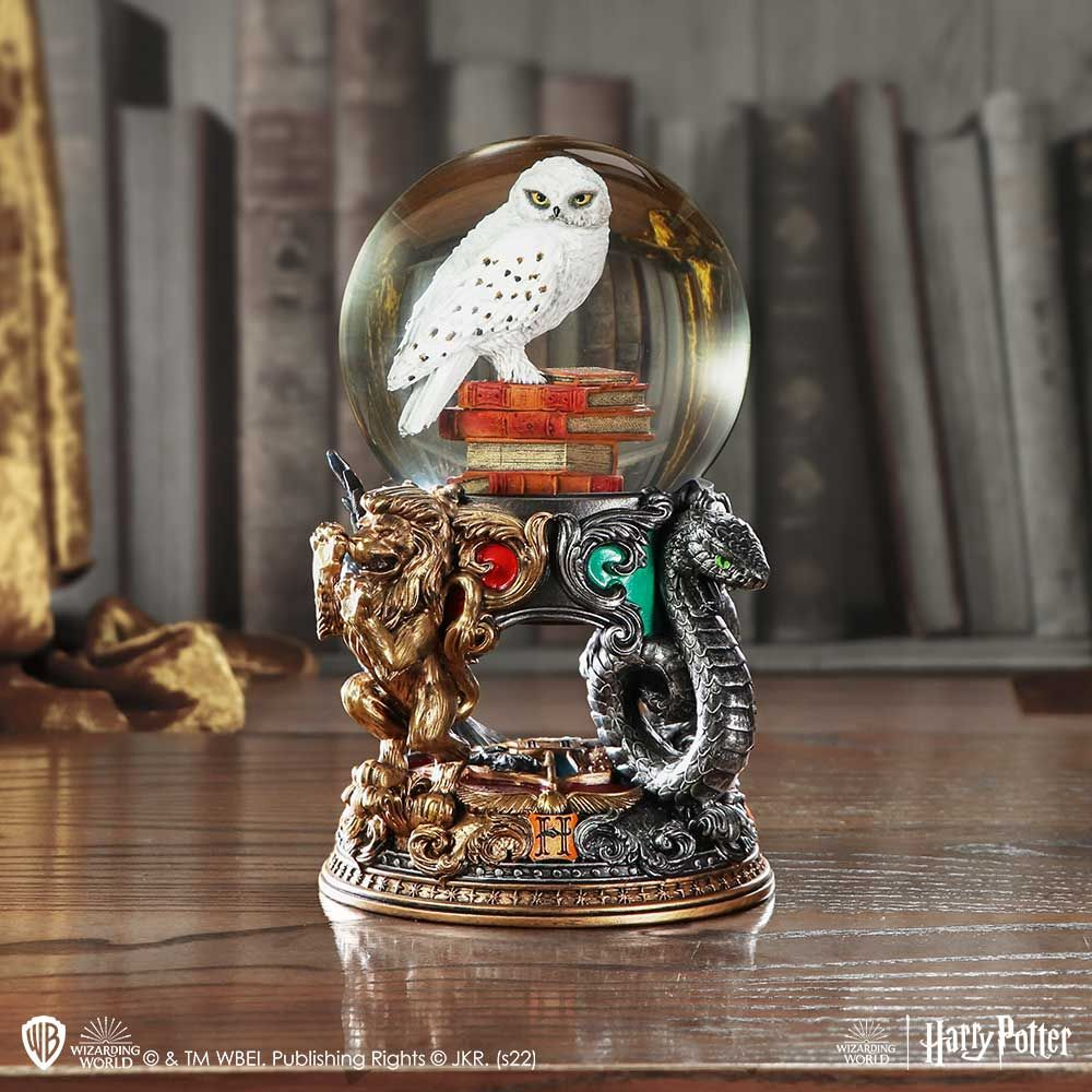 Snow globe with owl on books, lion and snake statues, wood table, books in background.