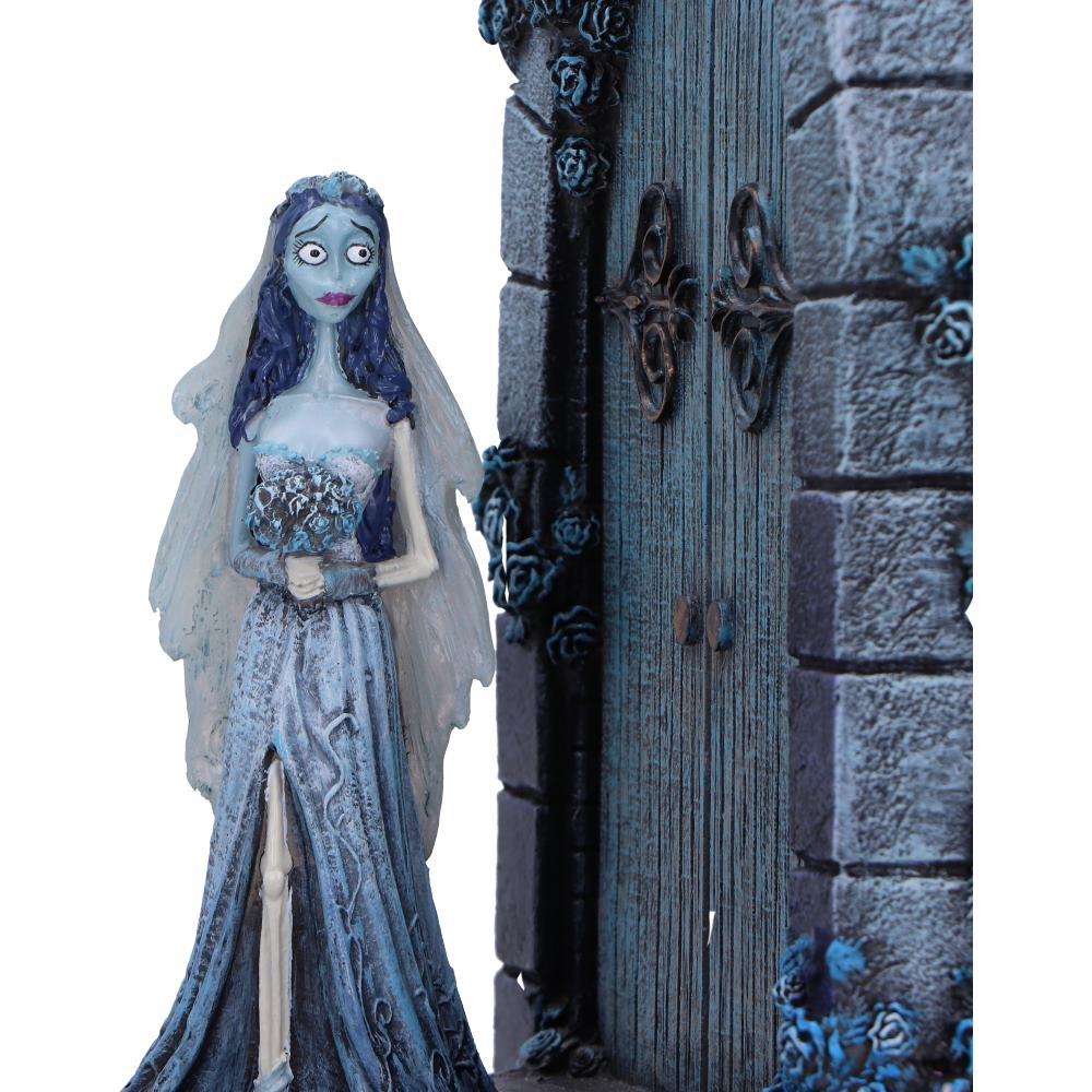 Corpse Bride-figuur staat bij een blauwe deur met rozen, draagt een blauwe jurk en sluier, houdt bloemen vast.