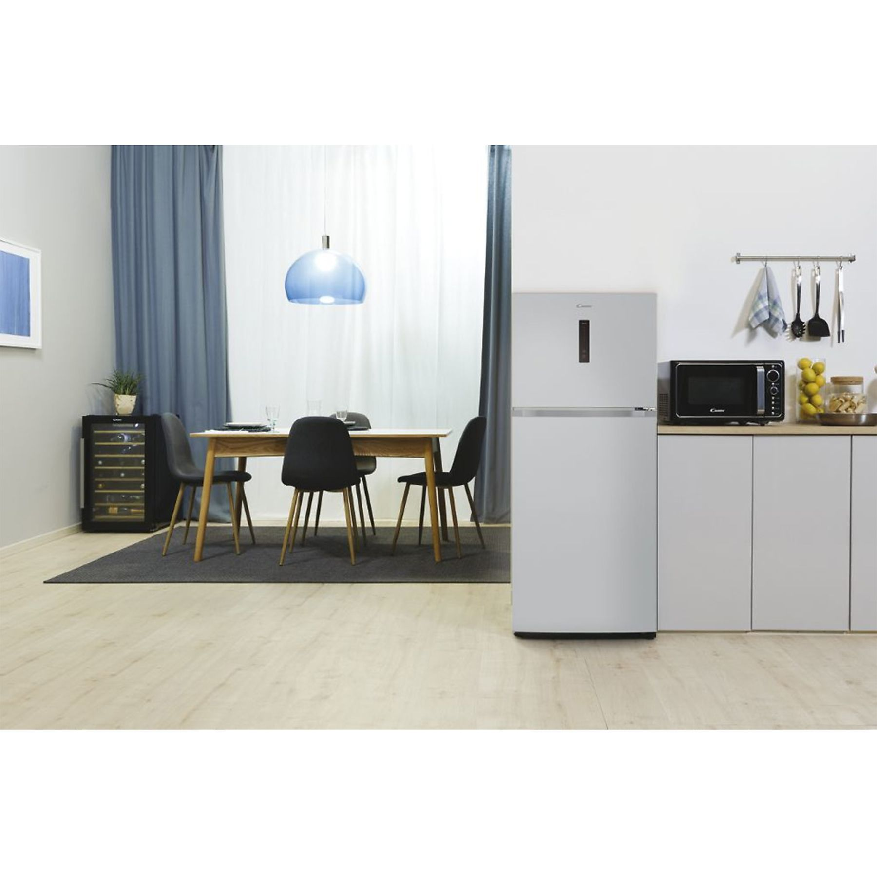 Interno cucina con frigorifero, microonde, tavolo, sedie e una lampada a sospensione blu.