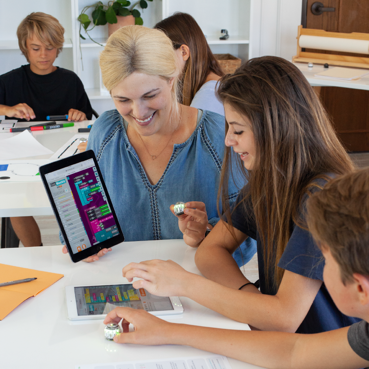 A woman and children looking at tablets. They are in a bright room, learning together.