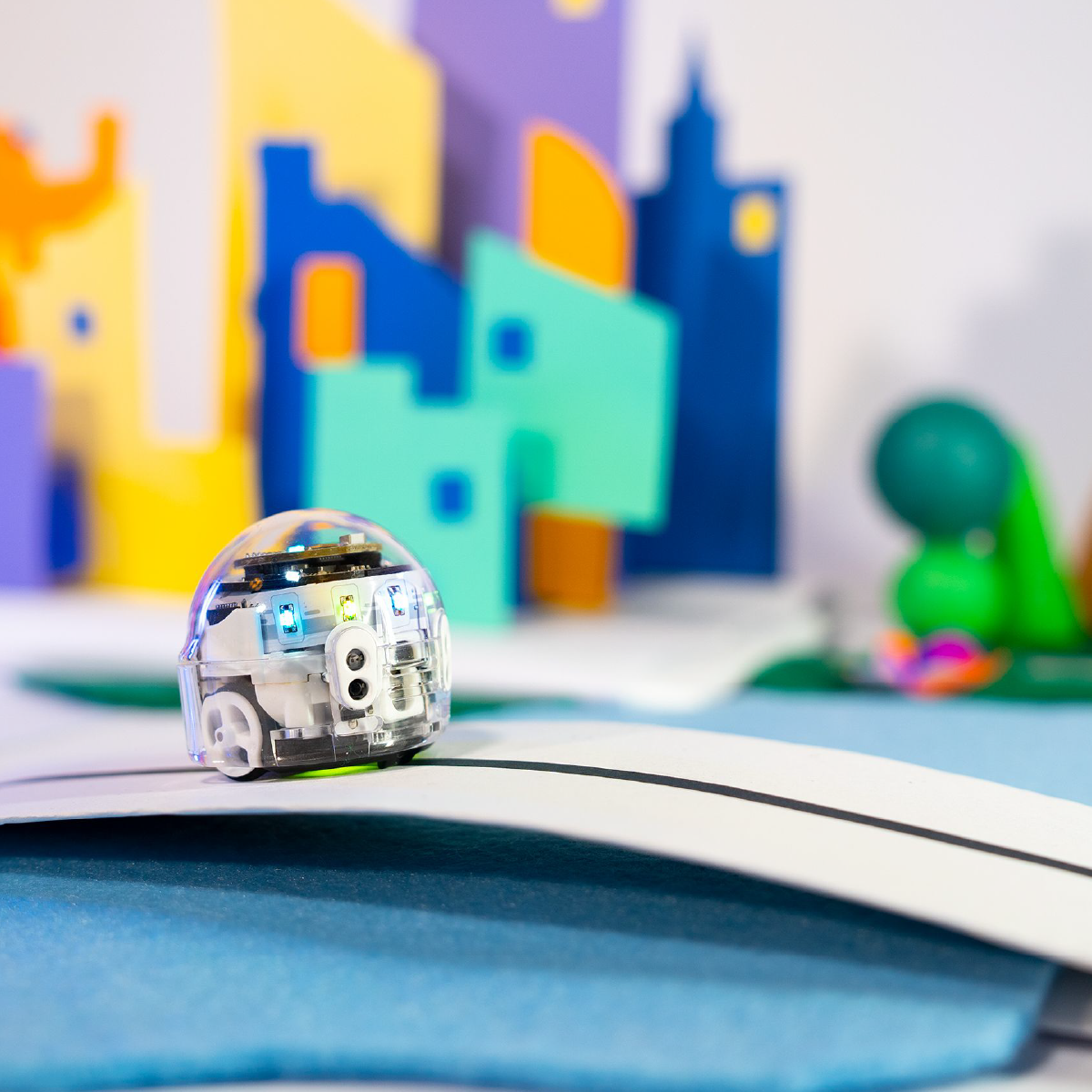 A toy robot on a white line, with a city and colorful shapes in the background.